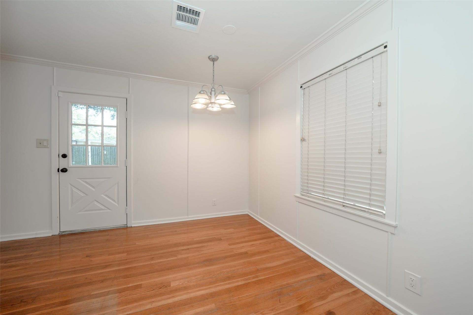 9519 Val Verde Street, Houston, TX 77063 Bright dining area with hardwood floors, white walls, and a ceiling light fixture. Features a window with blinds and a door leading outside, creating a cozy and inviting space.