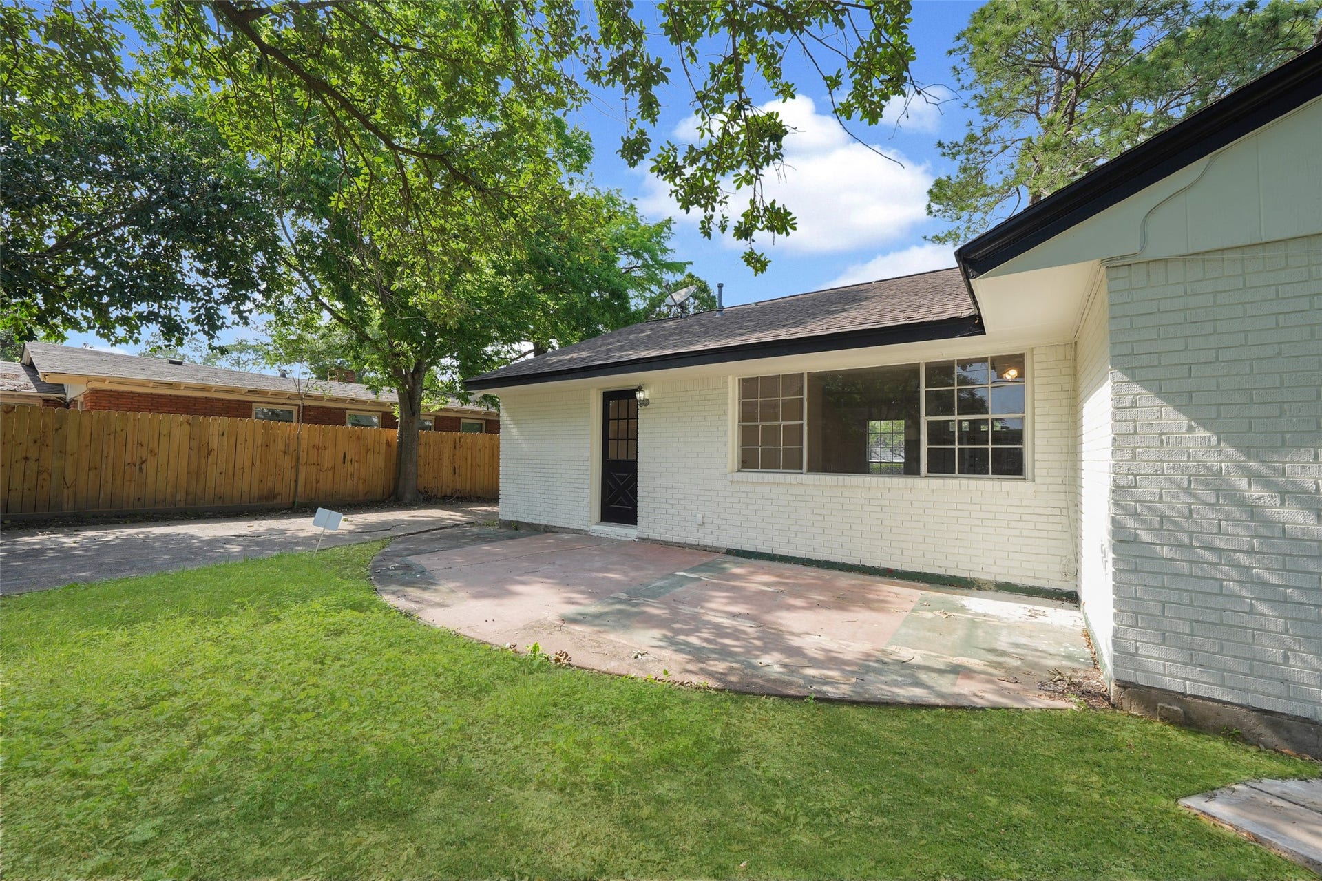 9519 Val Verde Street, Houston, TX 77063 Charming backyard with a spacious patio and lush lawn, surrounded by a wooden fence for privacy. The house features a white brick exterior and a large window for natural light. Perfect for outdoor relaxation and entertaining.