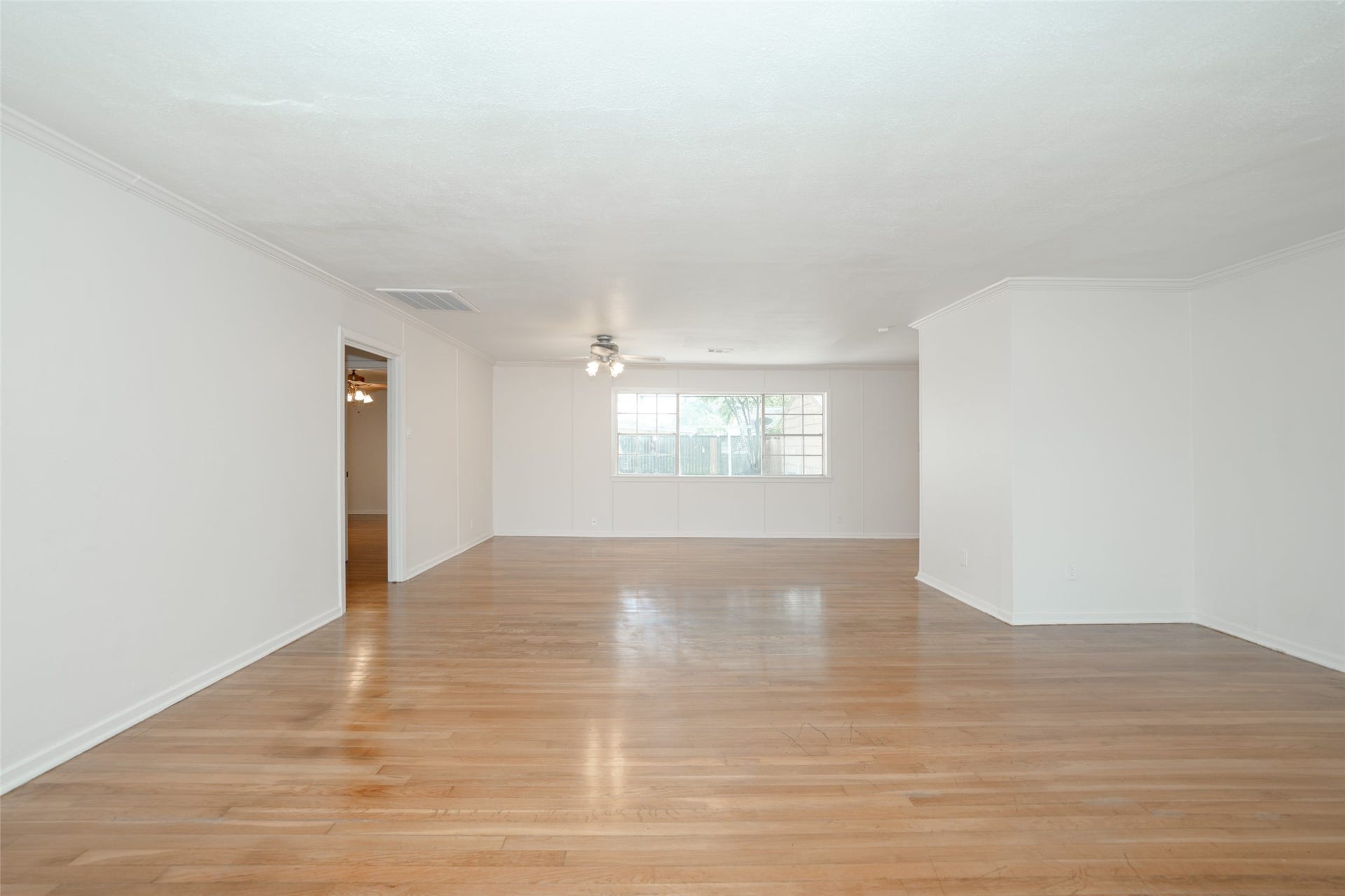 9519 Val Verde Street, Houston, TX 77063 This photo showcases a spacious, bright living area with light hardwood floors and white walls. A large window allows natural light to fill the room, and a ceiling fan is centrally located. An open doorway leads to an adjacent room, offering a versatile layout for a home buyer.