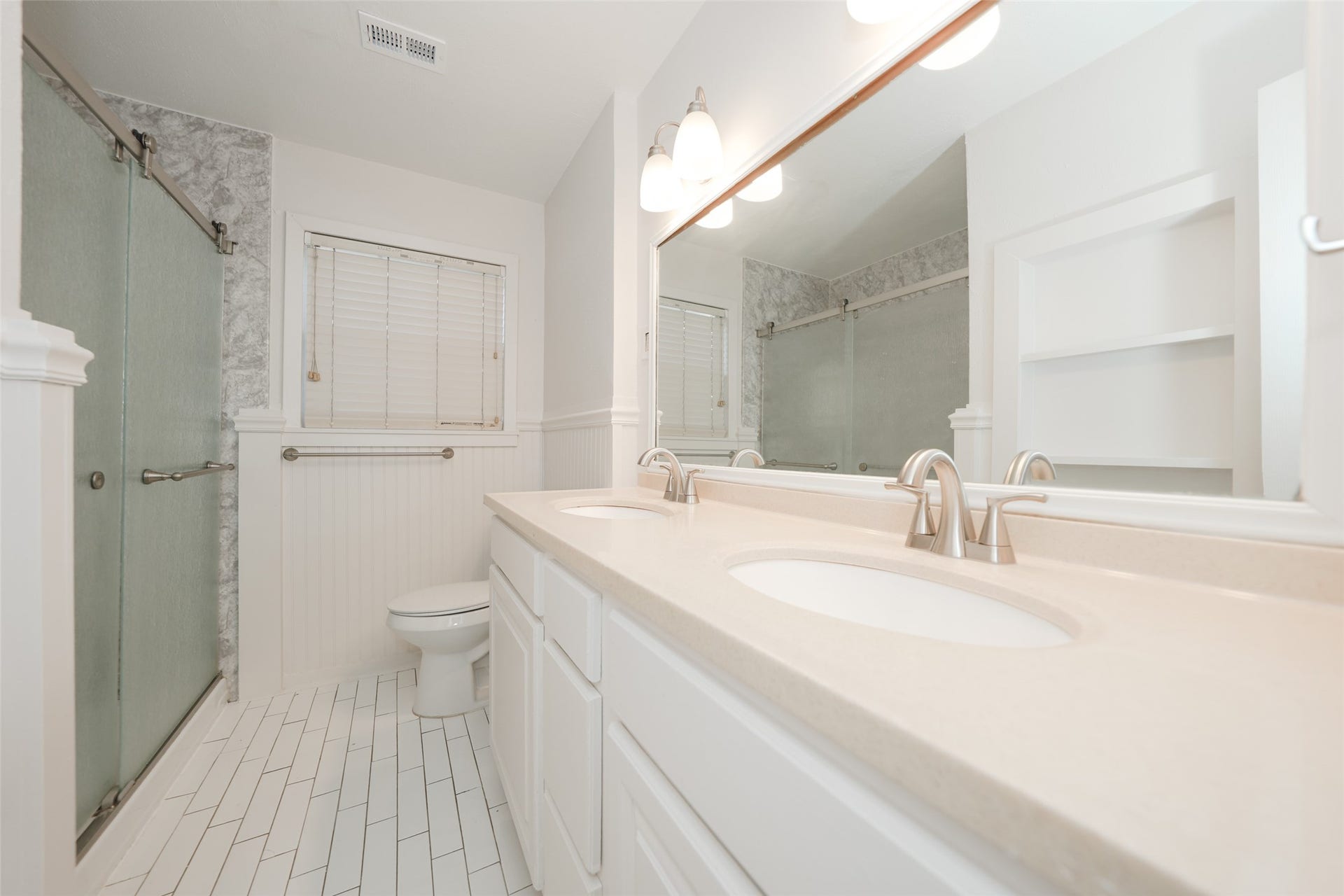 9519 Val Verde Street, Houston, TX 77063 This bathroom features a modern, clean design with a spacious double vanity, elegant light fixtures, and a large mirror. It includes a glass-enclosed shower and neutral tile flooring, creating a bright and inviting space.