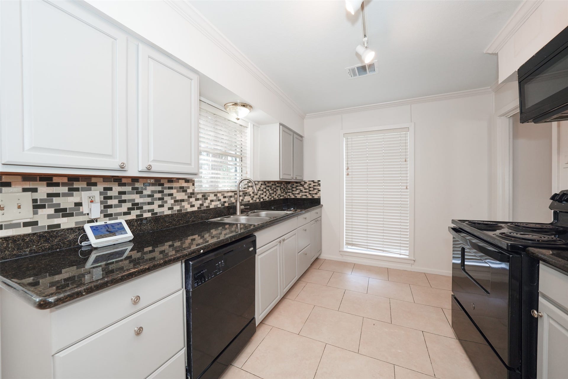 9519 Val Verde Street, Houston, TX 77063 This kitchen features sleek black appliances, white cabinetry, and a modern tile backsplash. It has granite countertops and large windows providing plenty of natural light.