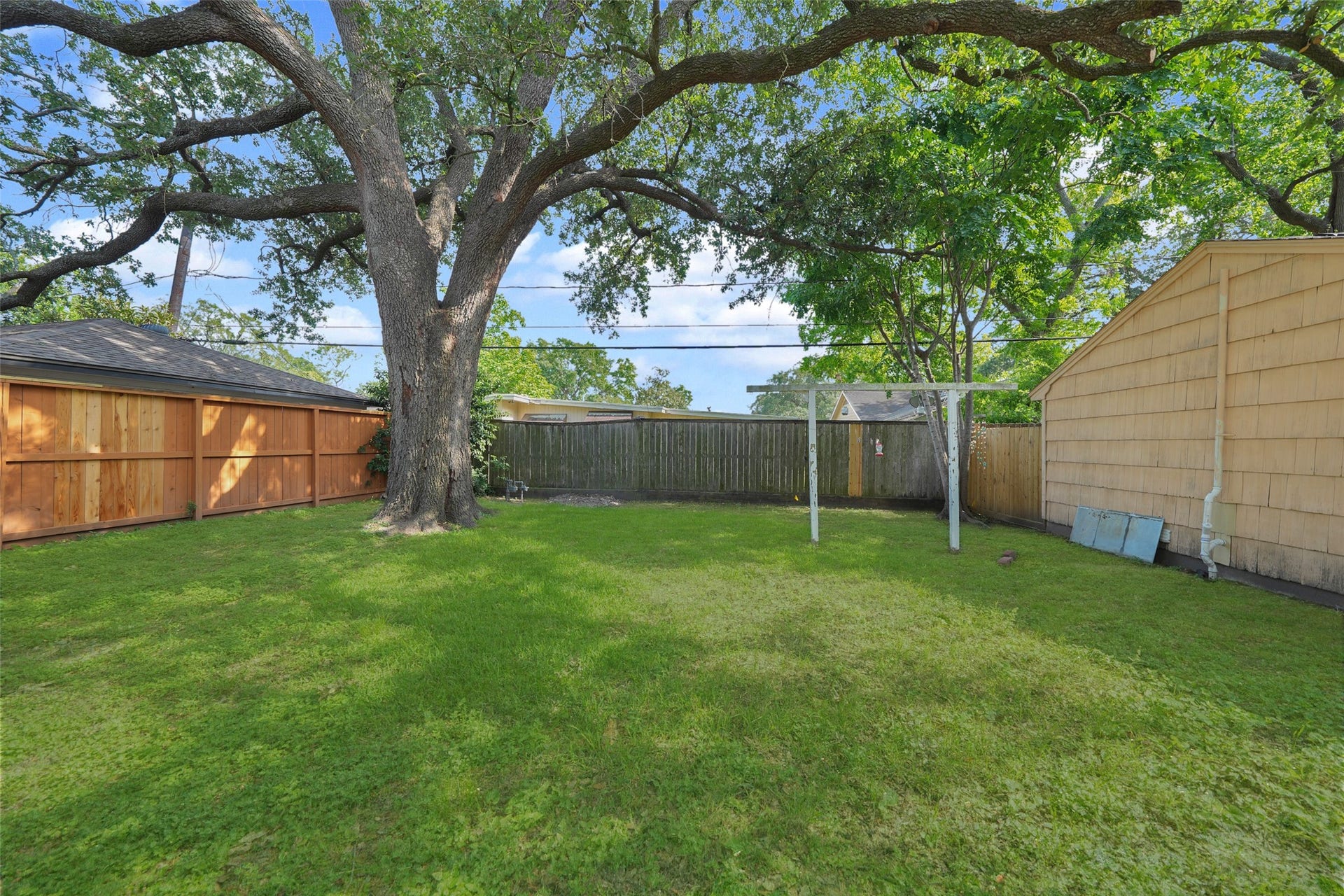 9519 Val Verde Street, Houston, TX 77063 Spacious backyard with lush grass, a large tree providing shade, and surrounded by a wooden fence. Ideal for outdoor activities and relaxation.