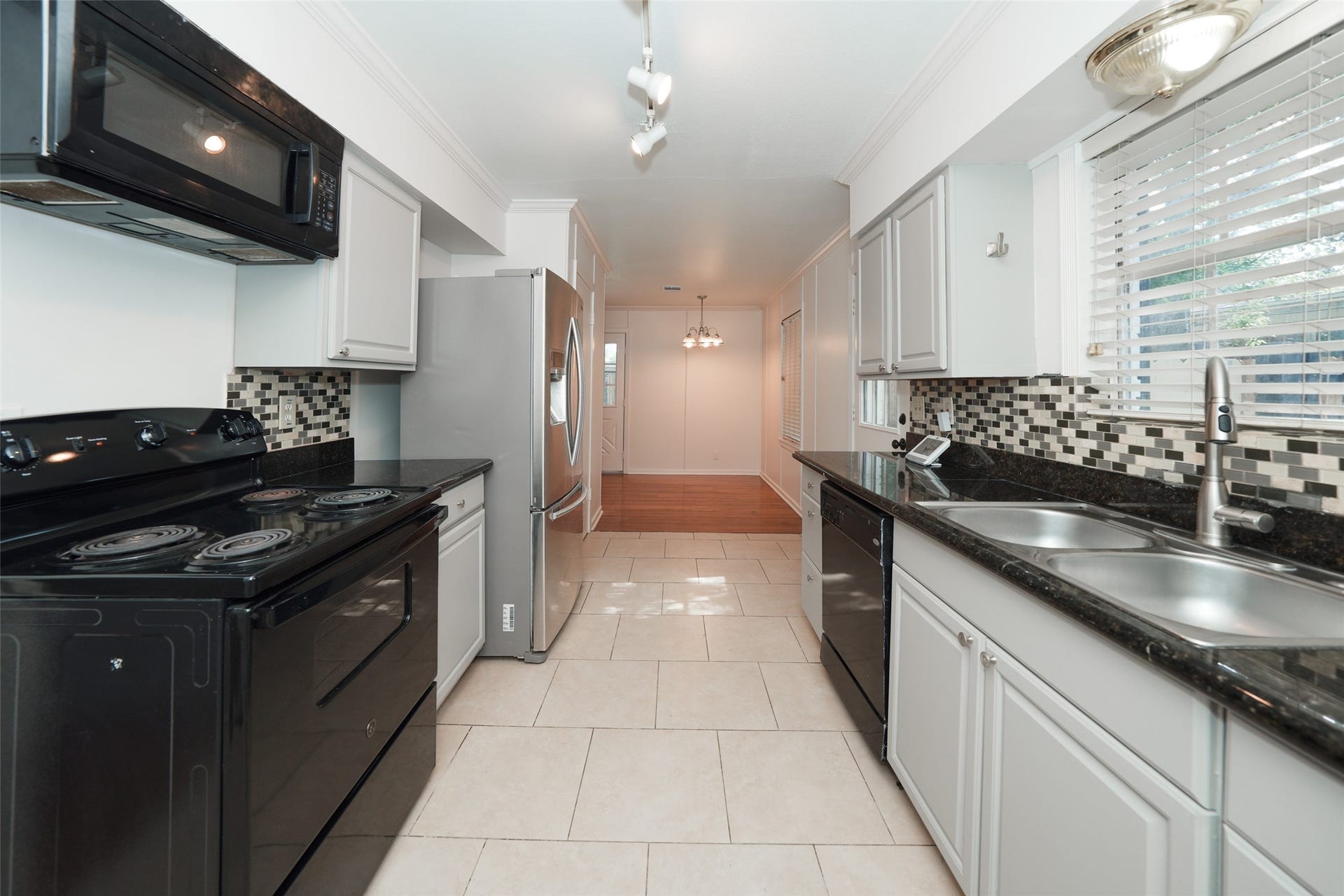 9519 Val Verde Street, Houston, TX 77063 This kitchen features modern appliances, black countertops, and a stylish tile backsplash. It has bright white cabinetry, a double sink, and ample natural light from large windows, creating a welcoming and functional space.
