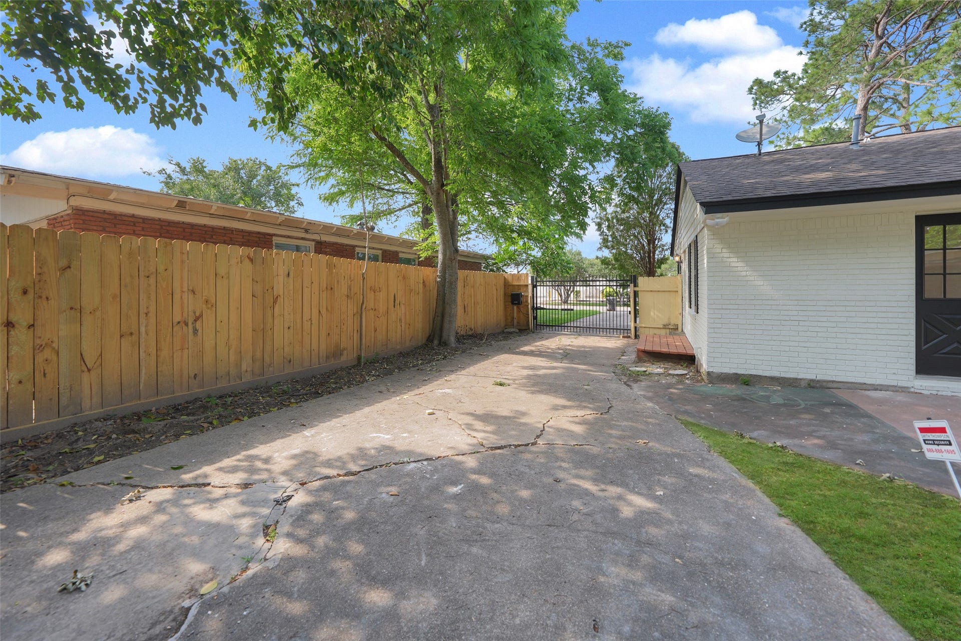 9519 Val Verde Street, Houston, TX 77063 A spacious driveway leads to a fenced backyard, offering privacy and potential for outdoor activities. The area is partially shaded by mature trees, providing a pleasant environment.