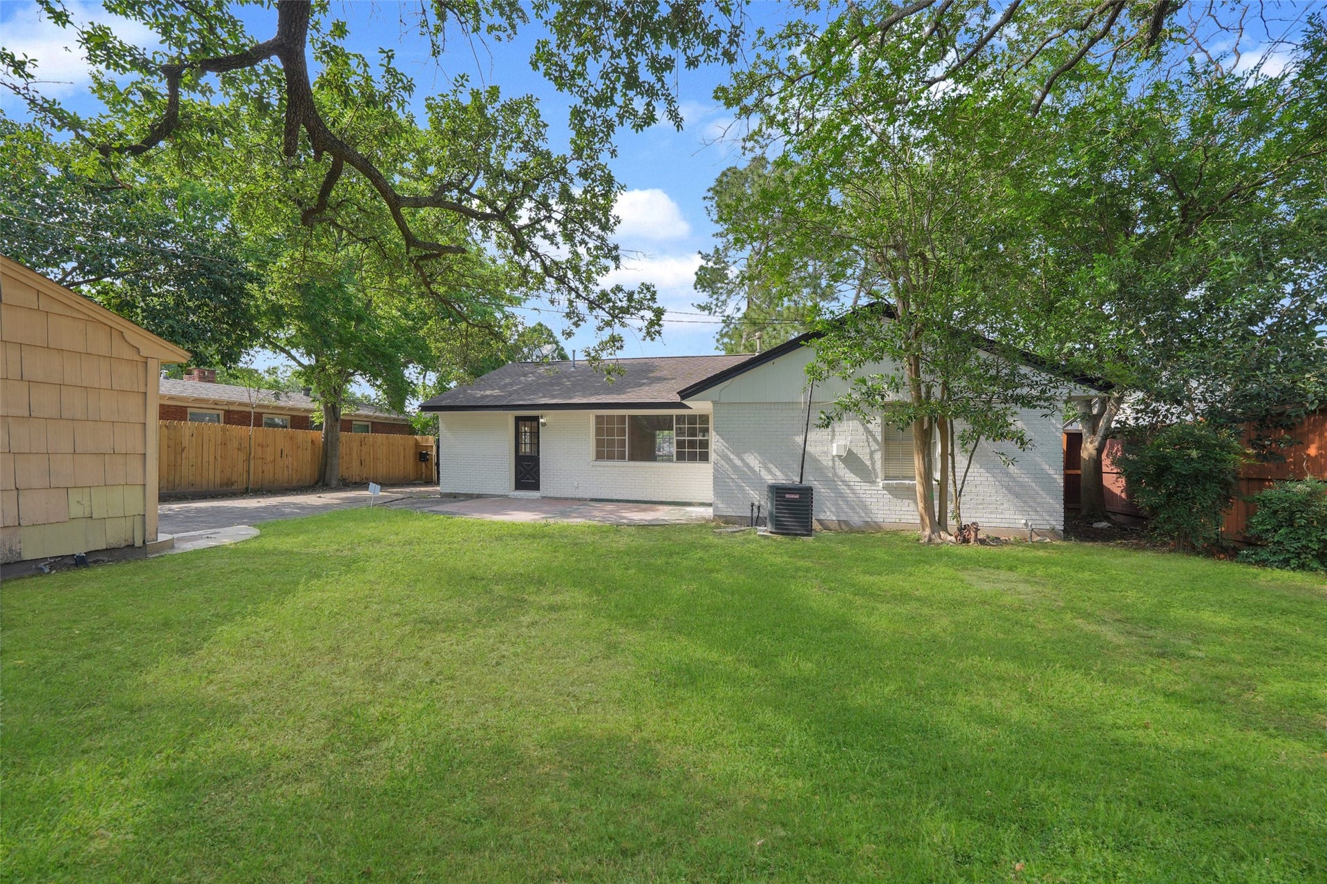 9519 Val Verde Street, Houston, TX 77063 Charming backyard with lush green lawn, mature trees providing shade, and a cozy white house. Perfect for outdoor activities and relaxation.