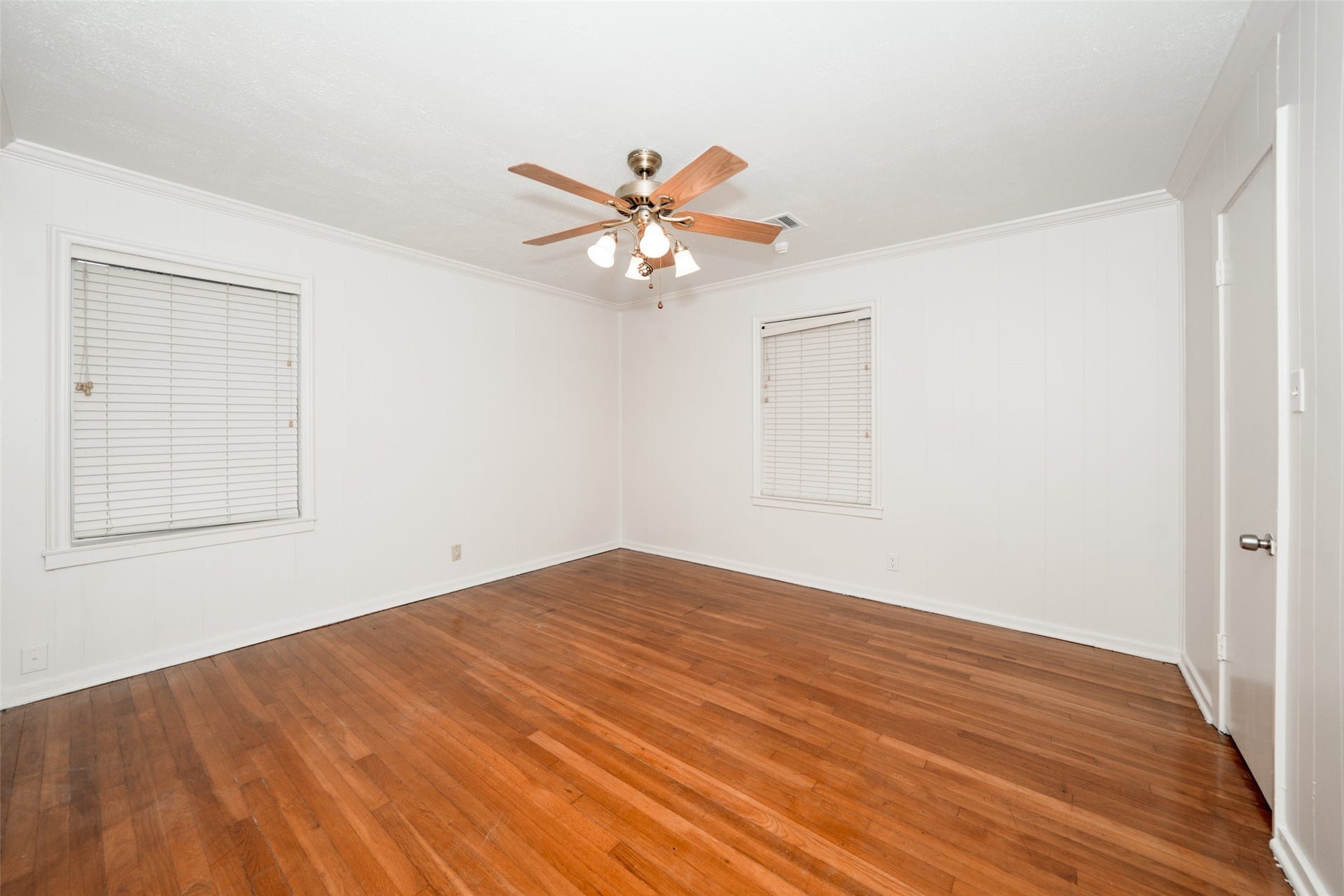 9519 Val Verde Street, Houston, TX 77063 This room features hardwood flooring, white walls, and two windows with blinds. It has a ceiling fan with lights, creating a bright and airy feel.