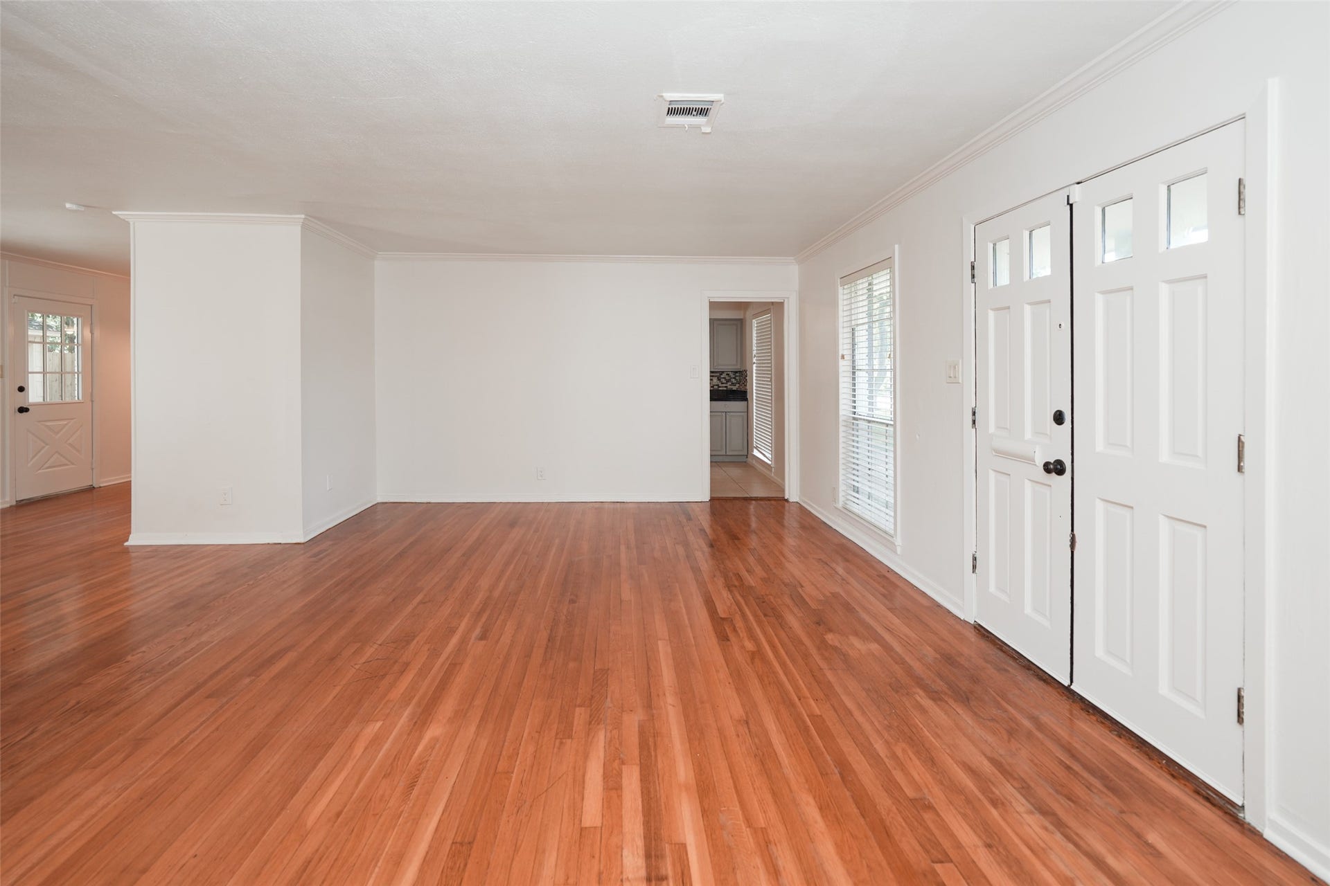 9519 Val Verde Street, Houston, TX 77063 This photo showcases a spacious, bright living room with hardwood floors, white walls, and a large front window. The room features a white front door and an open layout leading to the kitchen.