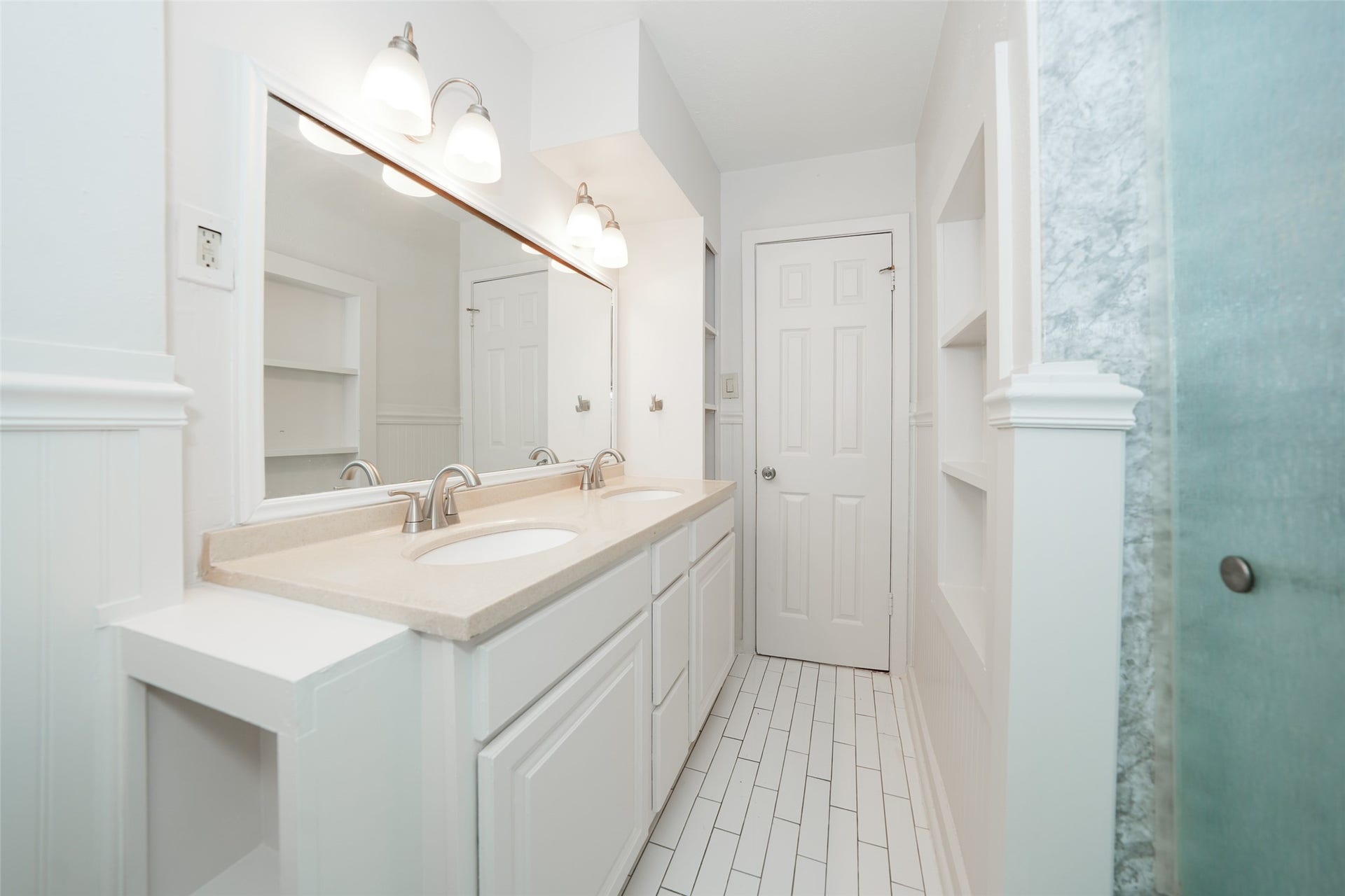 9519 Val Verde Street, Houston, TX 77063 This bright bathroom features a dual-sink vanity, modern fixtures, white tile flooring, ample storage with built-in shelves, and a frosted glass shower.