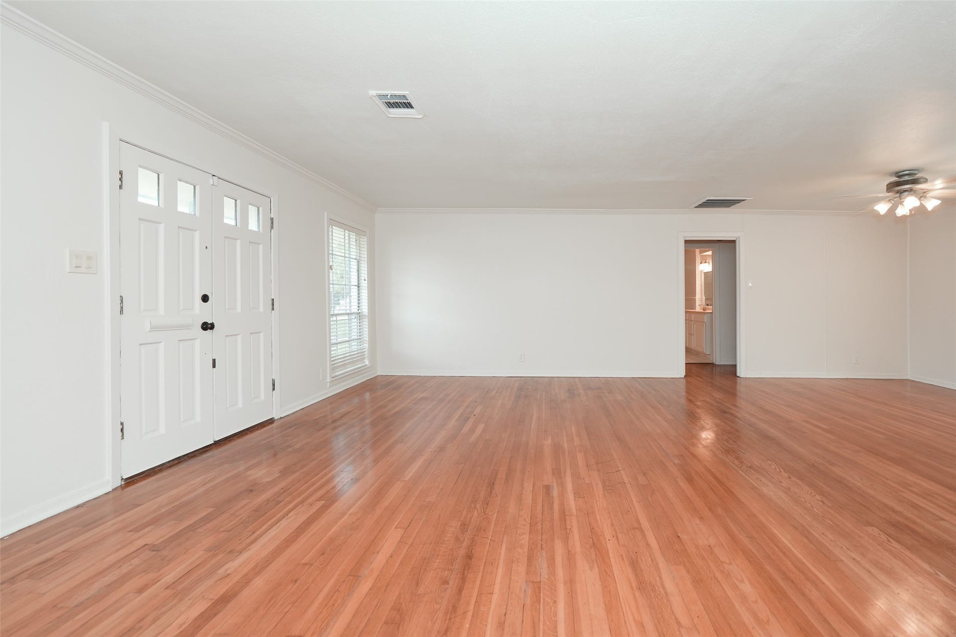 9519 Val Verde Street, Houston, TX 77063 Spacious living room with beautiful hardwood floors, neutral walls, and ample natural light from a large window. Features a ceiling fan and a view into the adjacent area, perfect for versatile living arrangements.