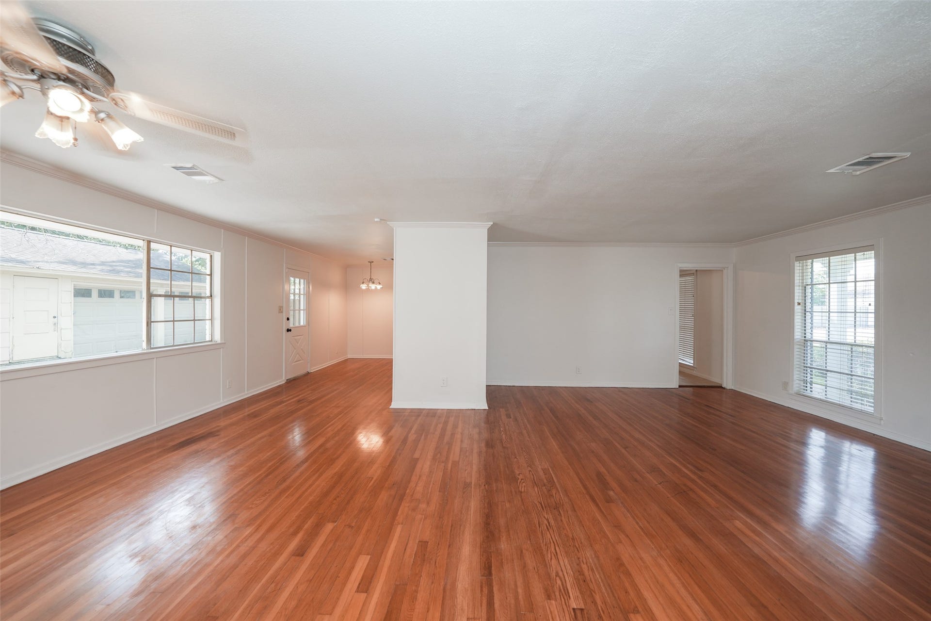 9519 Val Verde Street, Houston, TX 77063 This photo showcases a spacious living area with polished hardwood floors, large windows for natural light, and neutral-colored walls. The room has a ceiling fan and opens into an adjoining room, providing a versatile open-concept space.