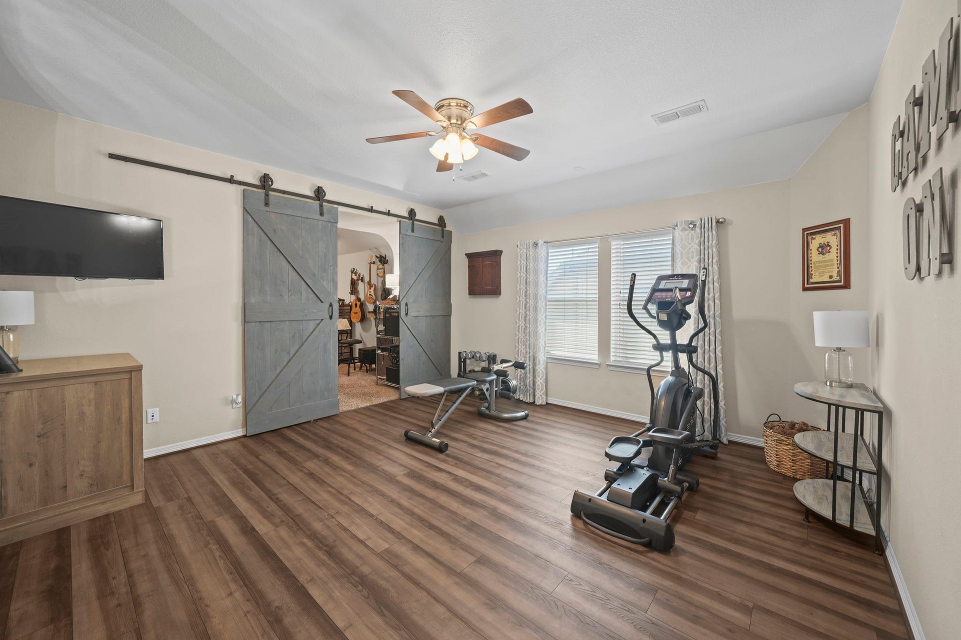 28107 Scenic Shore Lane, Fulshear, TX 77441 Spacious home gym with stylish barn doors, wood flooring, and ample natural light from large windows, perfect for workouts and relaxation.