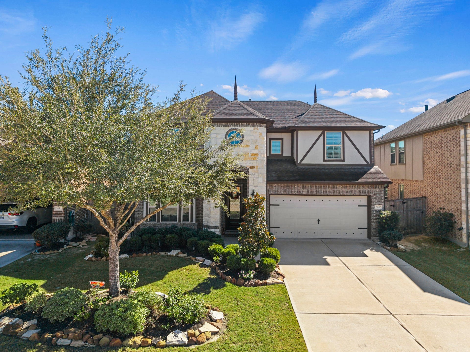 28107 Scenic Shore Lane, Fulshear, TX 77441 Charming two-story home with a spacious driveway, elegant brick and stone exterior, and well-manicured landscaping featuring mature trees and shrubs.