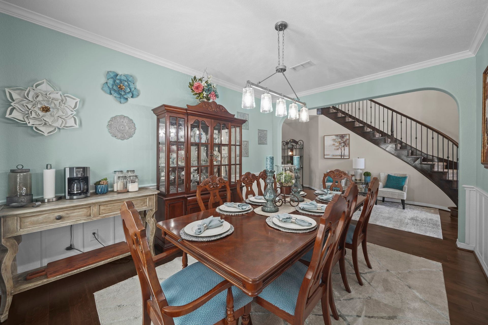 28107 Scenic Shore Lane, Fulshear, TX 77441 Elegant dining room with a grand wooden table, stylish chairs, and a striking chandelier. The space is accented by a beautiful china cabinet and decorative wall art, leading to an open staircase for a touch of sophistication.