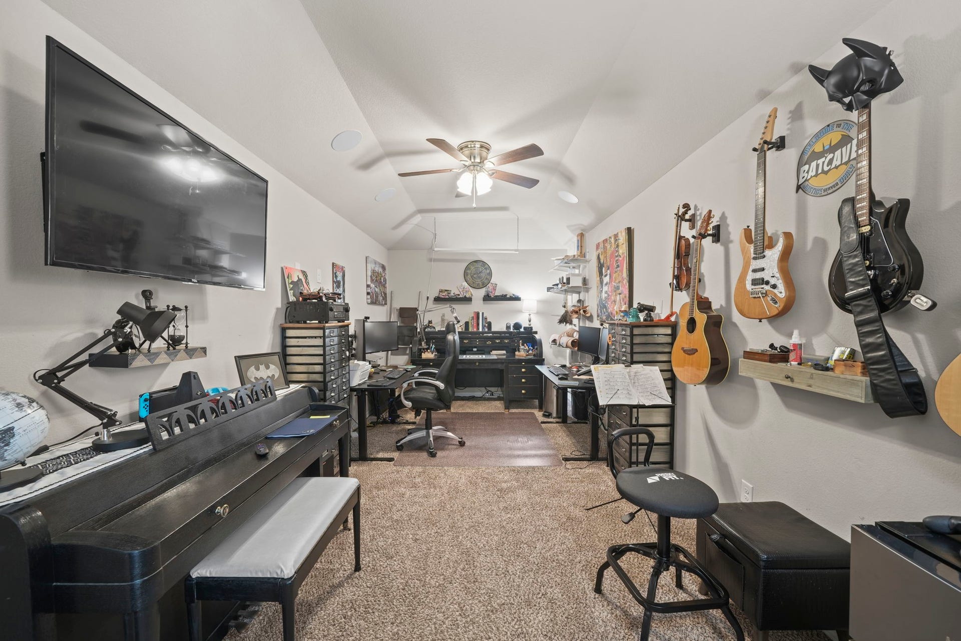 28107 Scenic Shore Lane, Fulshear, TX 77441 Versatile music and workspace featuring wall-mounted guitars, a digital piano, ample shelving for storage, and a large TV, all under a ceiling fan for comfort.