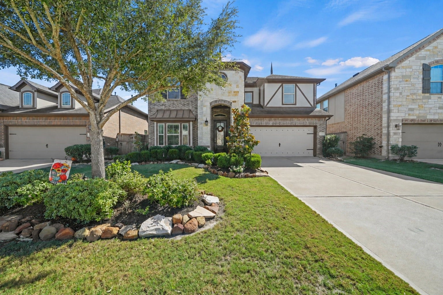 28107 Scenic Shore Lane, Fulshear, TX 77441 Charming two-story home with a stone facade and a welcoming front porch, nestled in a beautifully landscaped yard with mature trees and manicured shrubs.