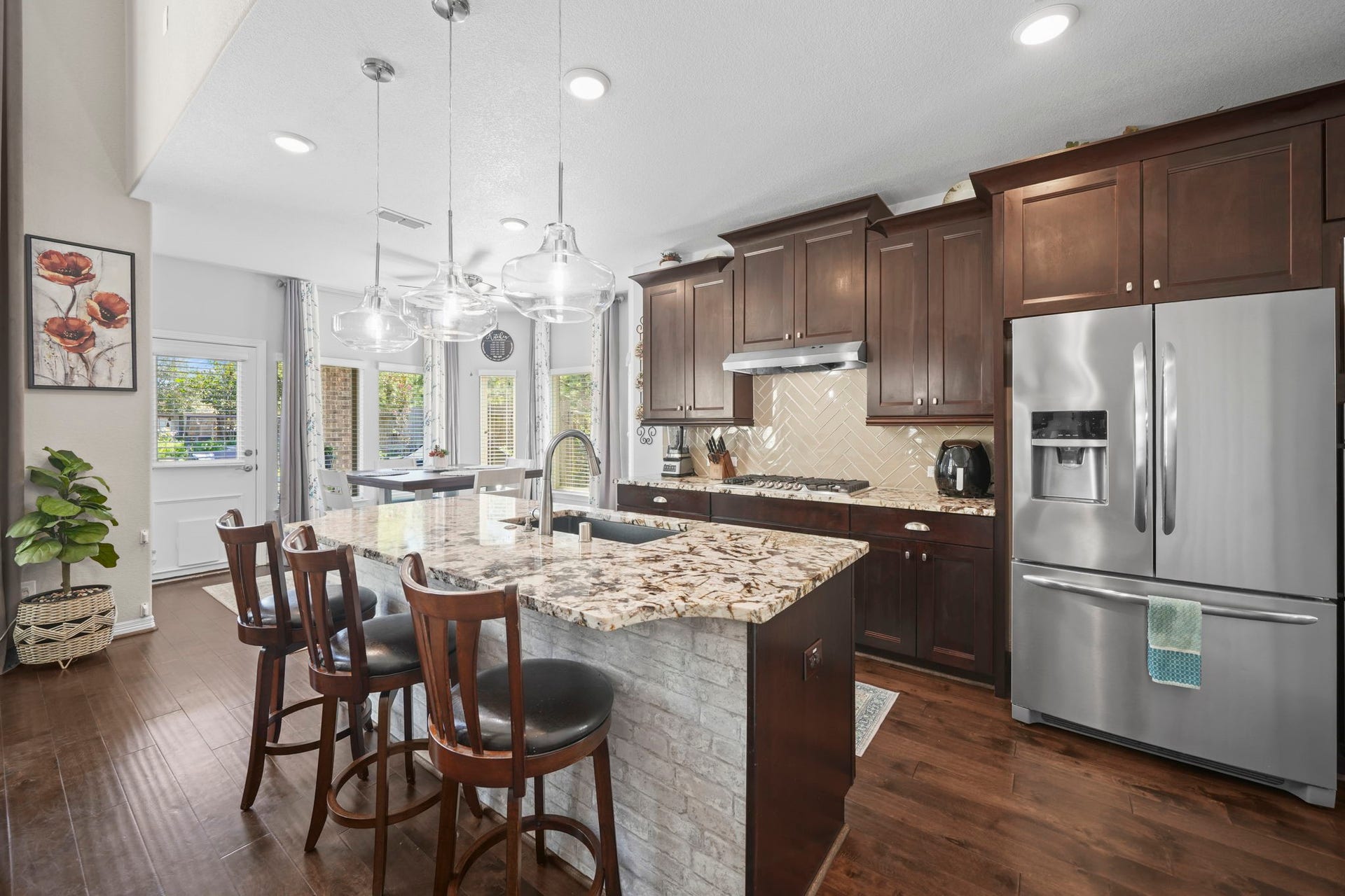 28107 Scenic Shore Lane, Fulshear, TX 77441 Elegant kitchen featuring rich wooden cabinetry, a large granite island with seating, and modern stainless steel appliances, all under stylish pendant lighting.