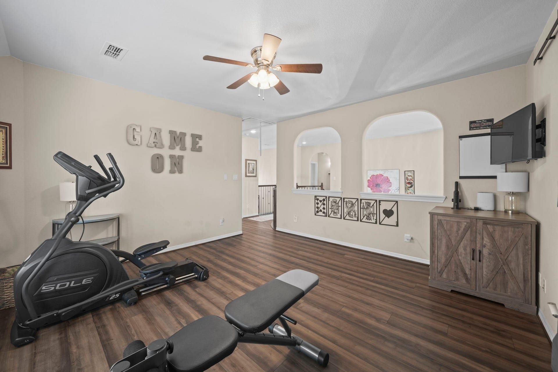 28107 Scenic Shore Lane, Fulshear, TX 77441 Spacious room with warm wood flooring, ideal for a home gym or entertainment area, featuring a ceiling fan, exercise equipment, and stylish decor.