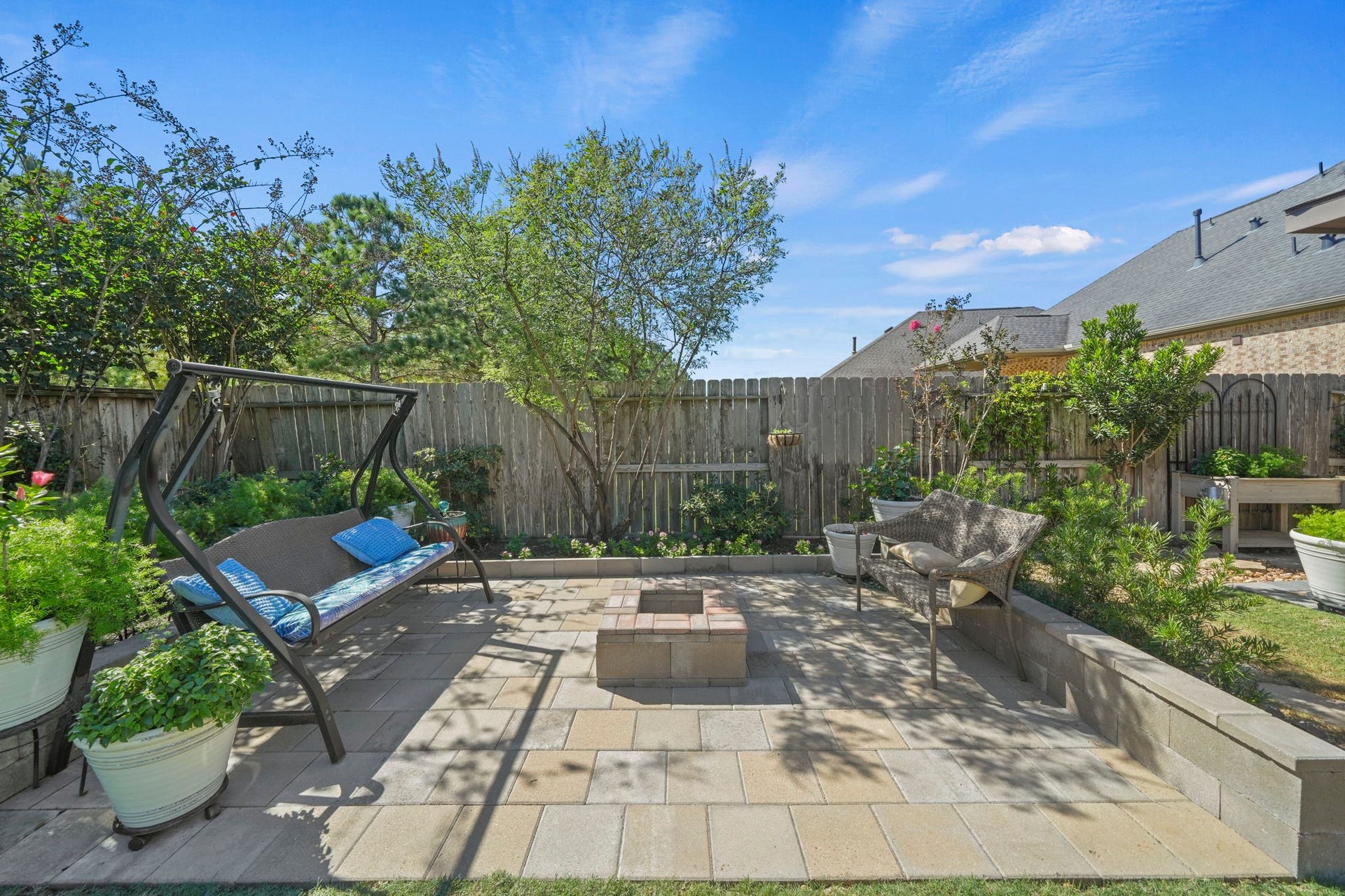 28107 Scenic Shore Lane, Fulshear, TX 77441 Charming backyard retreat featuring a cozy swing, lush greenery, and a central fire pit for outdoor relaxation and entertaining.