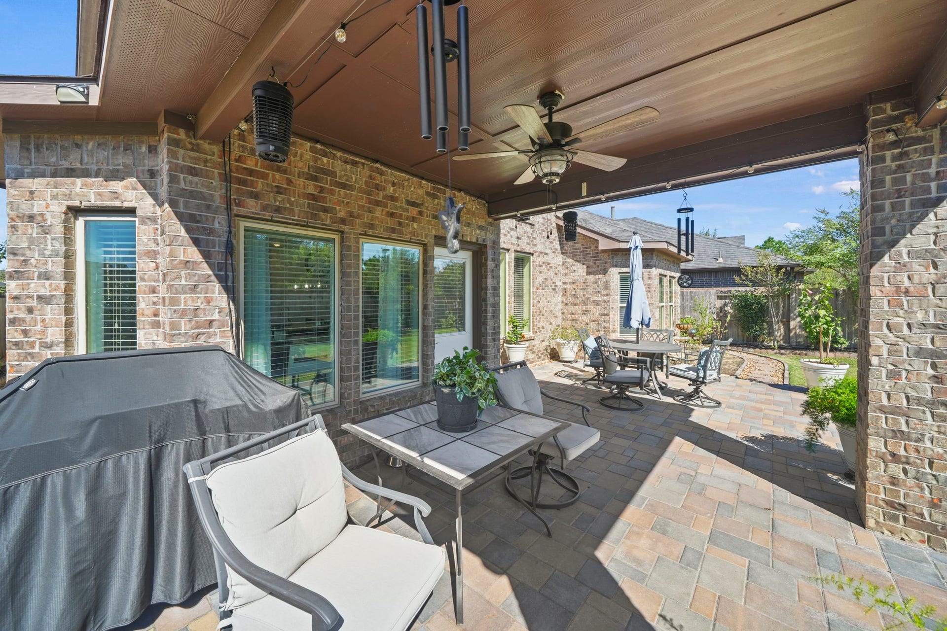 28107 Scenic Shore Lane, Fulshear, TX 77441 Charming brick patio featuring a covered seating area with a ceiling fan, perfect for outdoor dining and relaxation, complete with a barbecue grill and elegant landscaping.