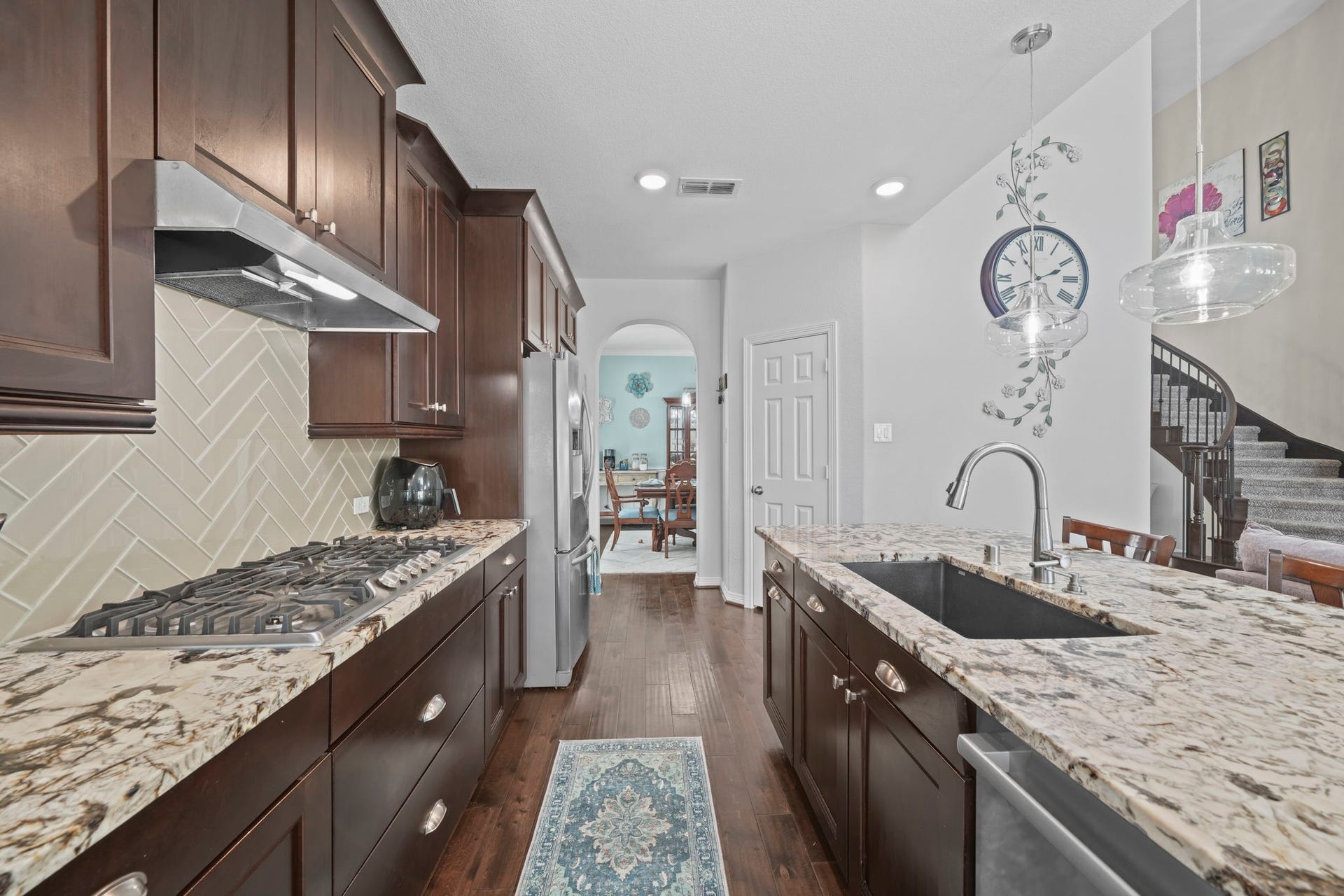 28107 Scenic Shore Lane, Fulshear, TX 77441 Elegant kitchen featuring rich dark wood cabinetry, granite countertops, and a stylish backsplash. The space is enhanced by modern pendant lighting and a spacious island with a built-in sink, perfect for entertaining.