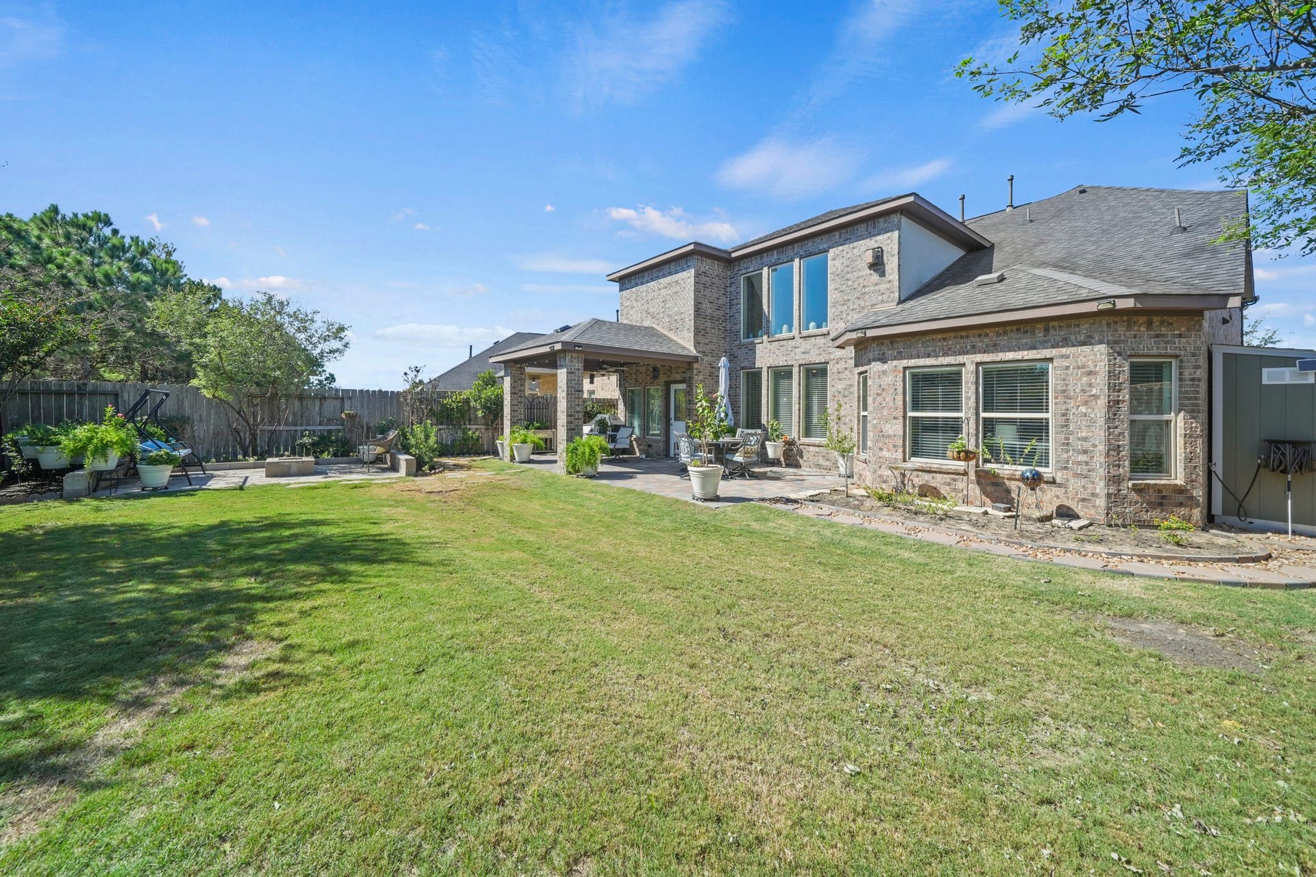 28107 Scenic Shore Lane, Fulshear, TX 77441 Spacious backyard with lush green lawn and a charming brick exterior, complemented by a covered patio perfect for outdoor entertaining.