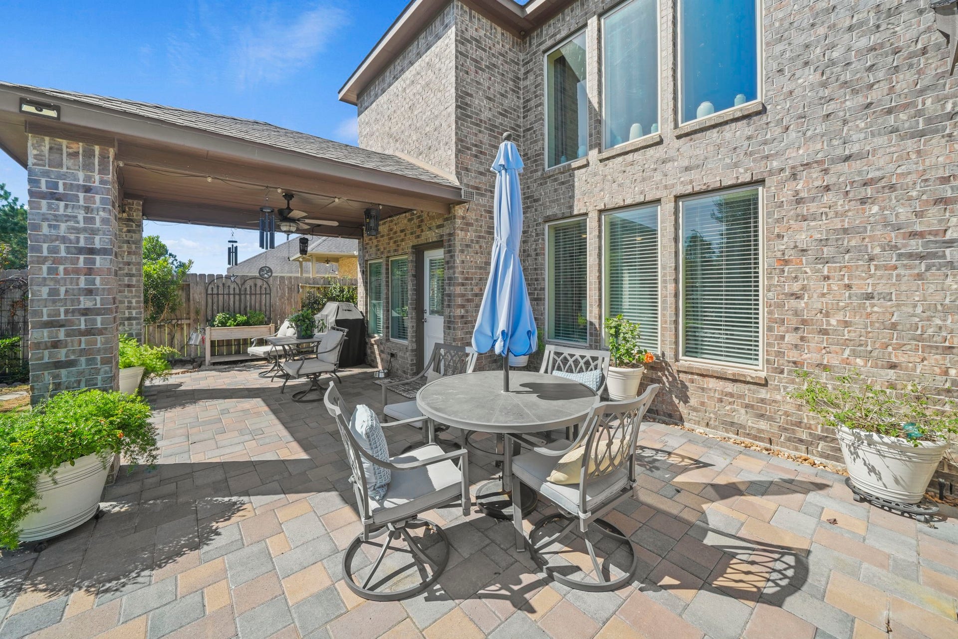 28107 Scenic Shore Lane, Fulshear, TX 77441 Charming brick patio with ample seating, perfect for outdoor dining and relaxation, featuring a covered area and lush potted greenery.
