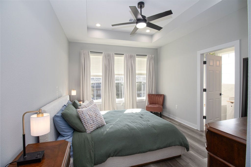 8415 Sunnyhill Street, #B, Houston, TX 77088 Spacious and inviting primary retreat featuring a decorative tray ceiling, modern ceiling fan, beautiful wood-look flooring, and three windows that fill the room with natural light.