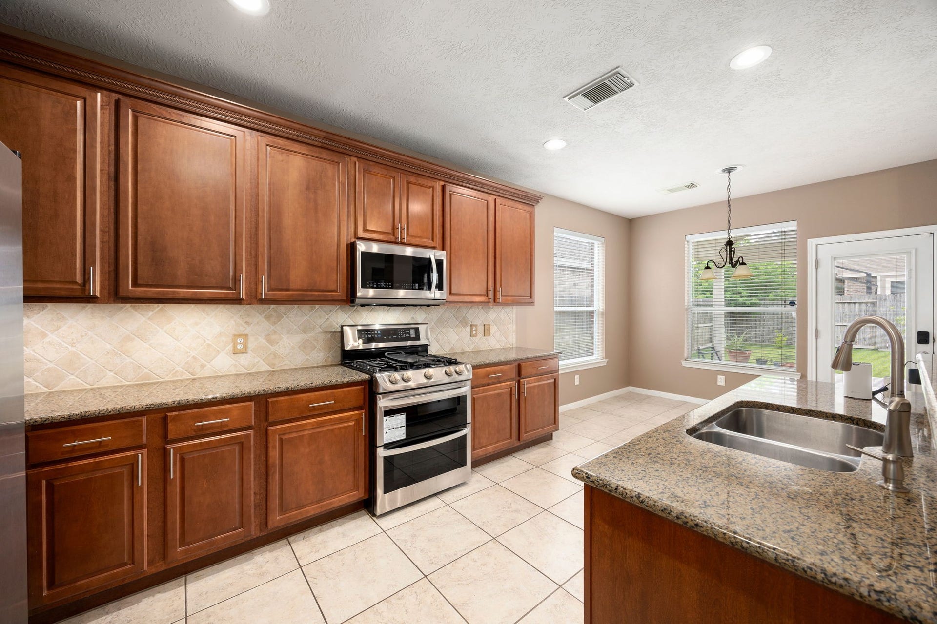 Beautifully appointed chef's kitchen featuring extensive warm wood cabinetry with elegant crown molding, durable granite countertops, and a classic tiled backsplash. High-end stainless steel appliances, including a gas range, make cooking a delight.