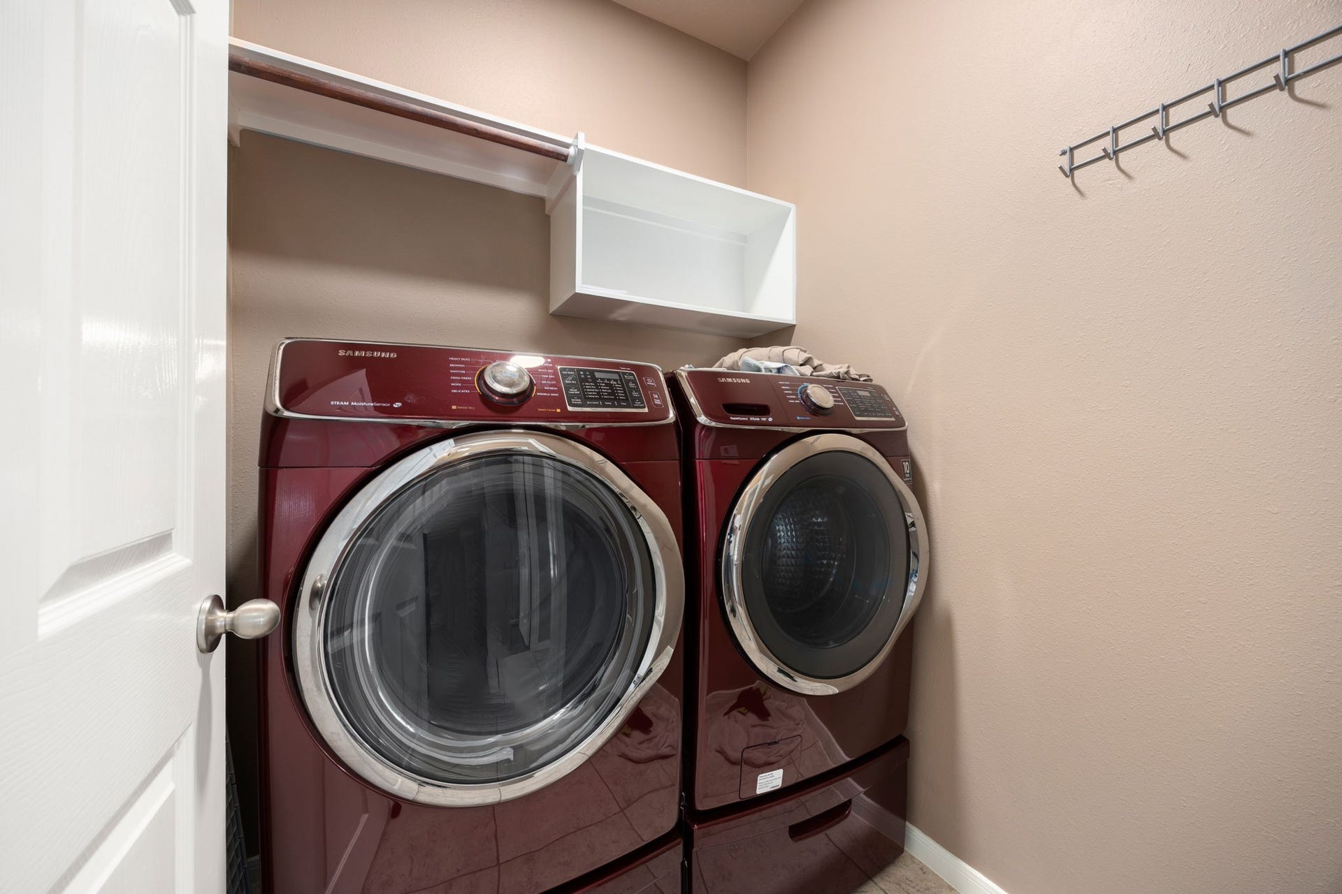 Convenient dedicated laundry room equipped with built-in storage cabinetry, a hanging clothing rod, and a wall-mounted drying rack. The functional layout maximizes efficiency with low-maintenance tile flooring.