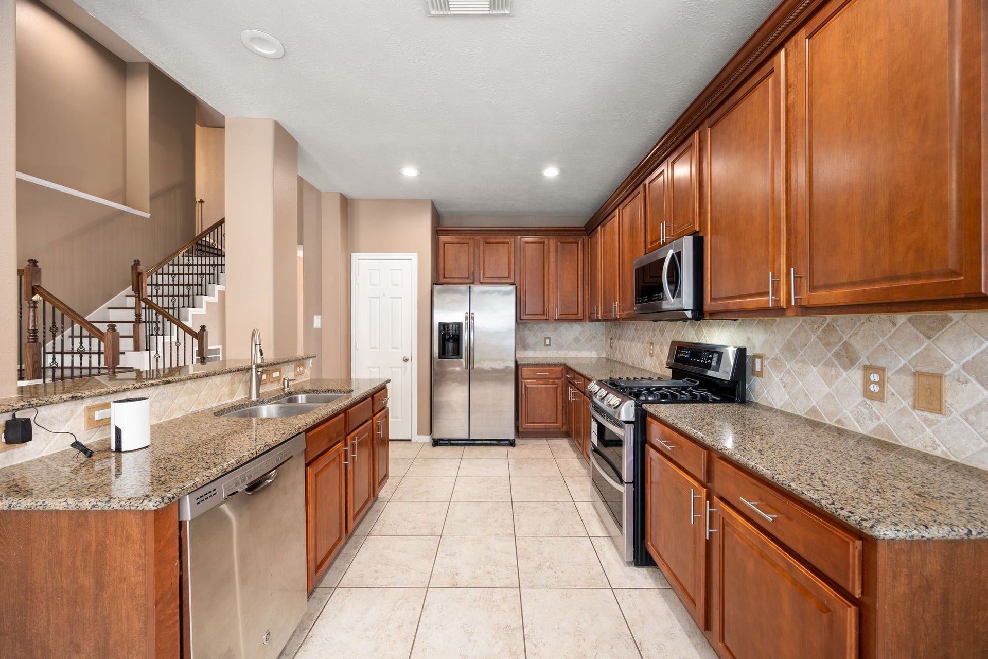 This view reveals an incredible amount of counter space and premium cabinetry with sleek hardware. The galley-style design is highly efficient, featuring matching stainless steel appliances, a built-in microwave, and a convenient pantry door at the far end.