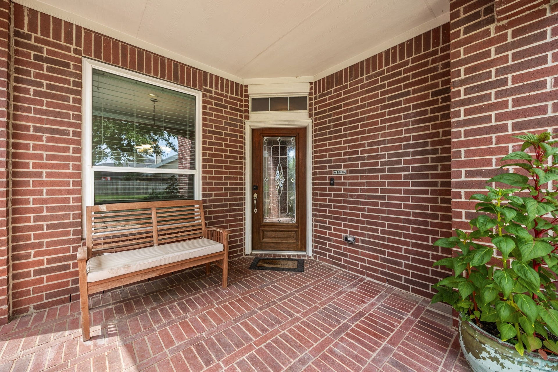 A charming covered front porch greets you with classic red brick flooring and matching brick walls. The elegant wooden front door features decorative leaded glass, creating an inviting first impression.