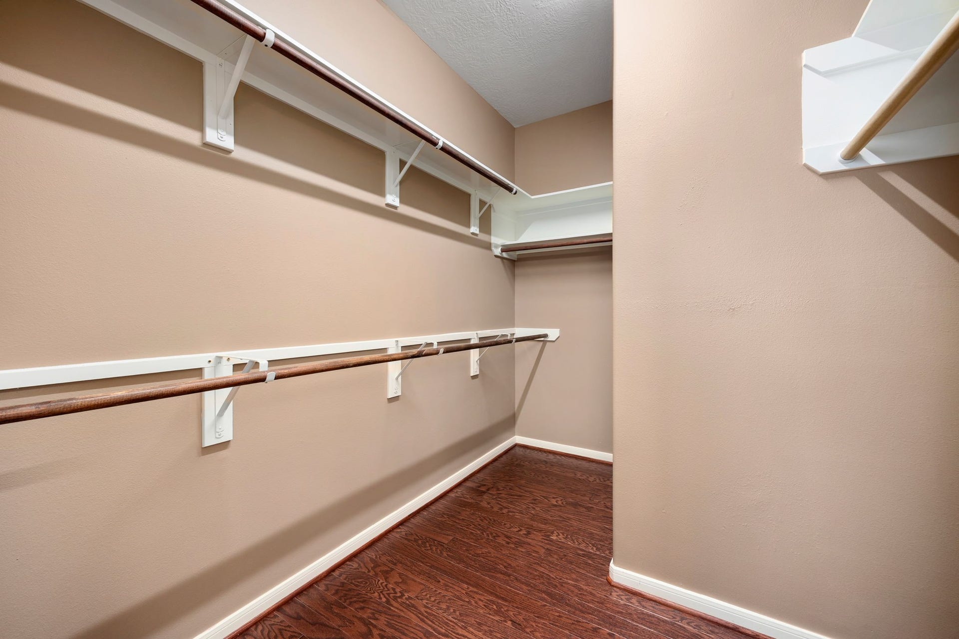Massive primary walk-in closet offering an abundance of storage space with multi-level hanging rods and integrated storage shelving. The premium wood-look flooring extends seamlessly into this oversized wardrobe retreat.