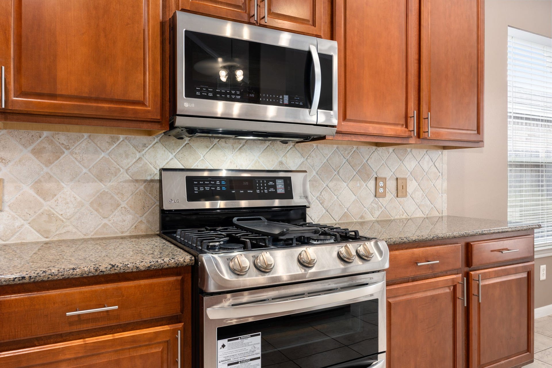 Home chefs will love the premium stainless steel gas range complete with an integrated griddle cooktop and a matching over-the-range microwave. The setup is beautifully framed by detailed stone-tile backsplash and rich wood cabinetry.