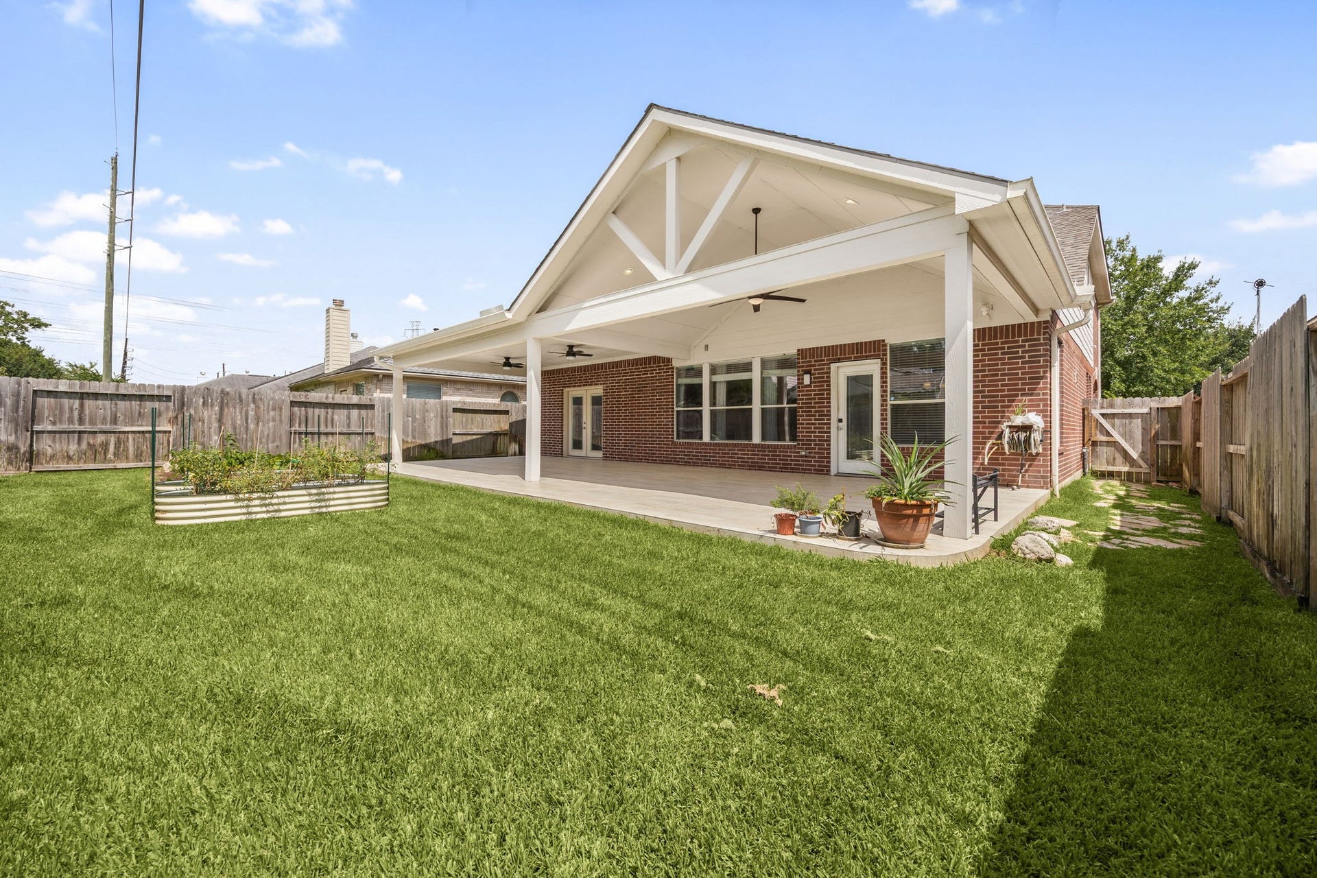 A fantastic perspective showcasing the full breadth of the lush, green backyard. The massive covered patio seamlessly bridges indoor and outdoor living, providing a stunning architectural focal point alongside a fully fenced lawn.