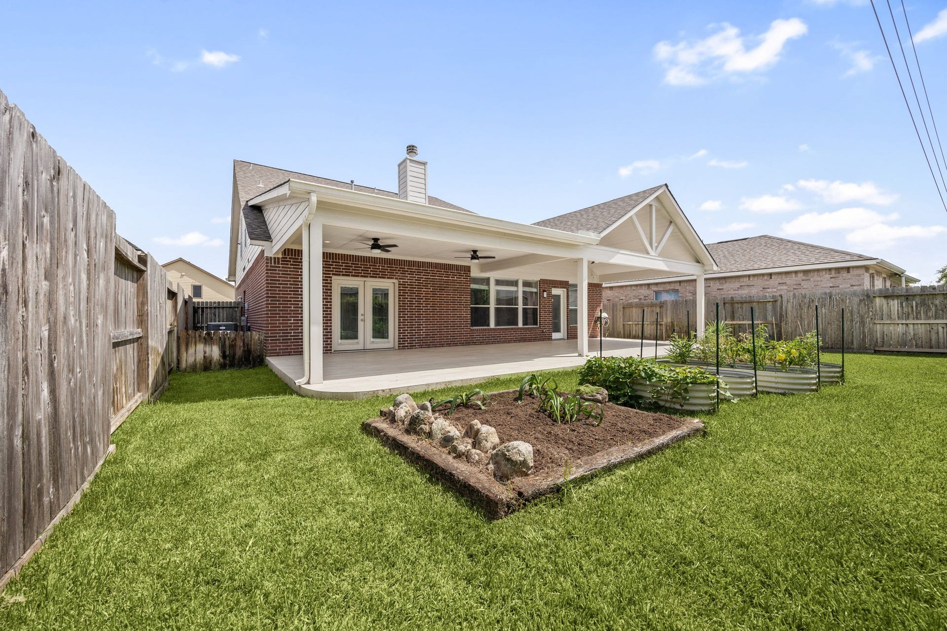 Fully fenced backyard featuring custom bordered garden beds, multi-tier raised garden boxes, and a massive covered patio.