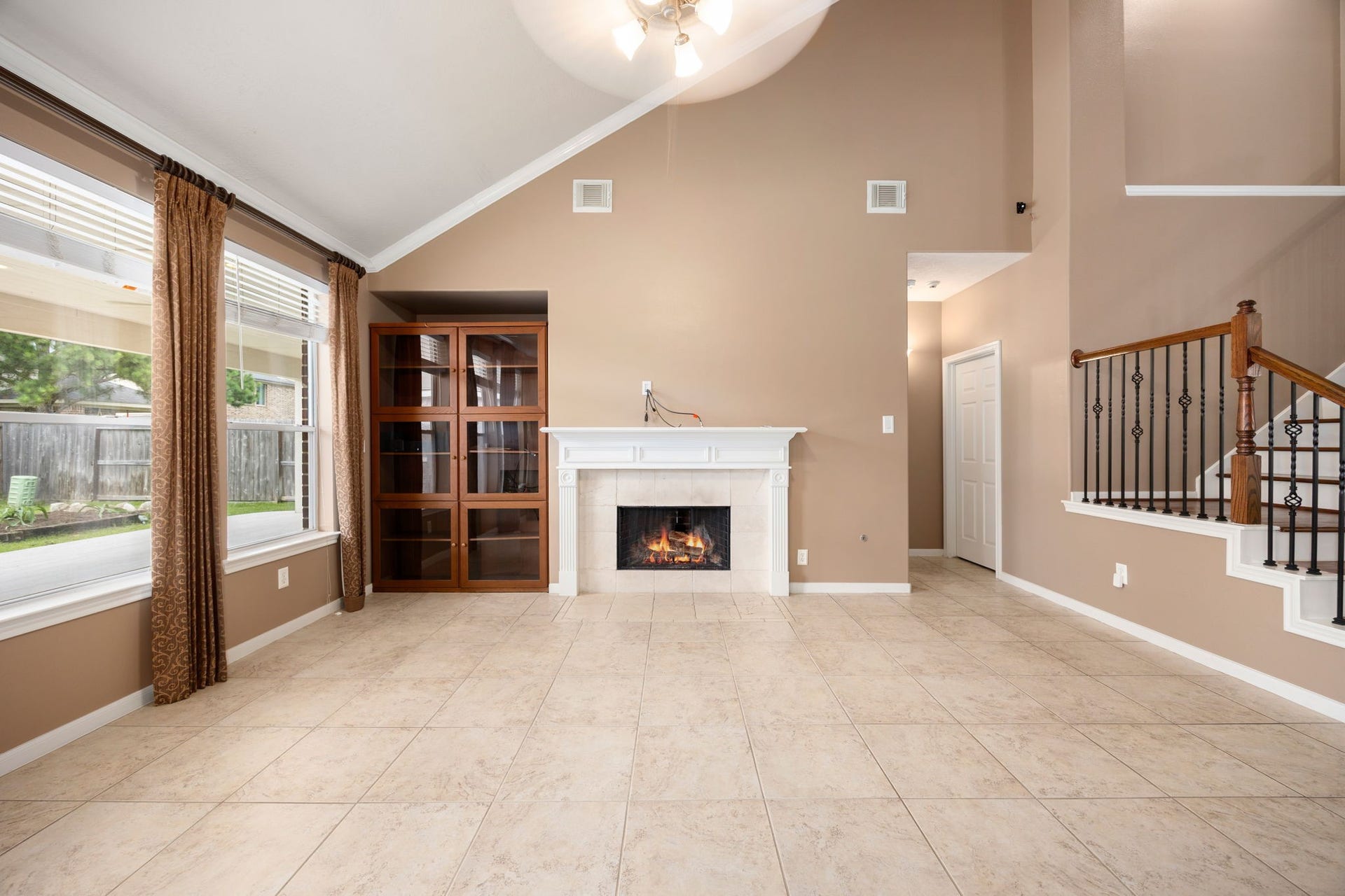 A closer look at the stunning family room centerpiece featuring a cozy fireplace with a detailed white mantel and a custom built-in media cabinet or bookcase. The soaring vaulted ceiling and open staircase create an exceptionally grand and airy atmosphere.