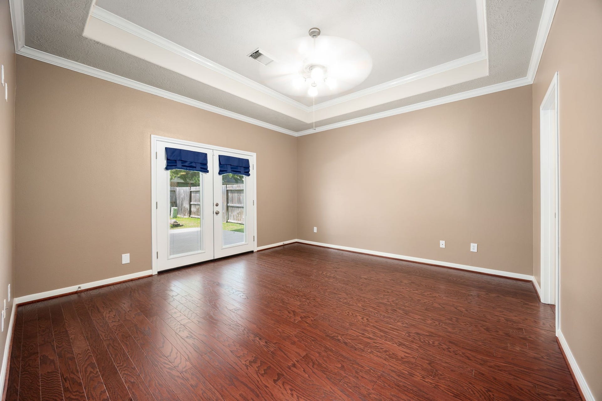Retreat to this spacious primary suite featuring beautiful tray ceilings accented by elegant crown molding. Rich wood-look plank flooring adds warmth, while double French doors open directly to the backyard for a private morning coffee spot.