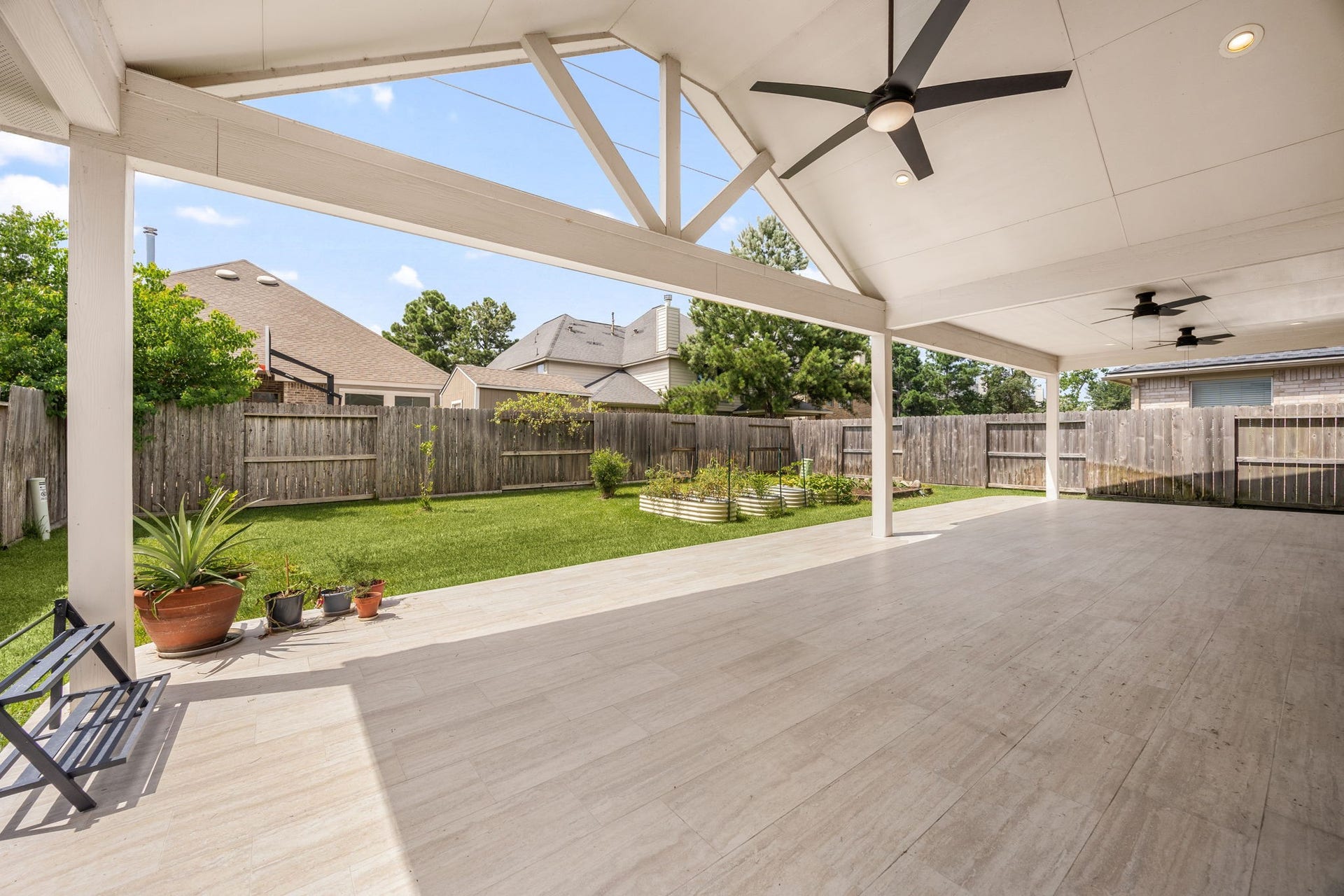 Step outside into your private backyard paradise! An enormous covered patio features an elegant vaulted ceiling with exposed truss details, ceiling fans, and premium tile flooring. The massive space overlooks a fully fenced green lawn.