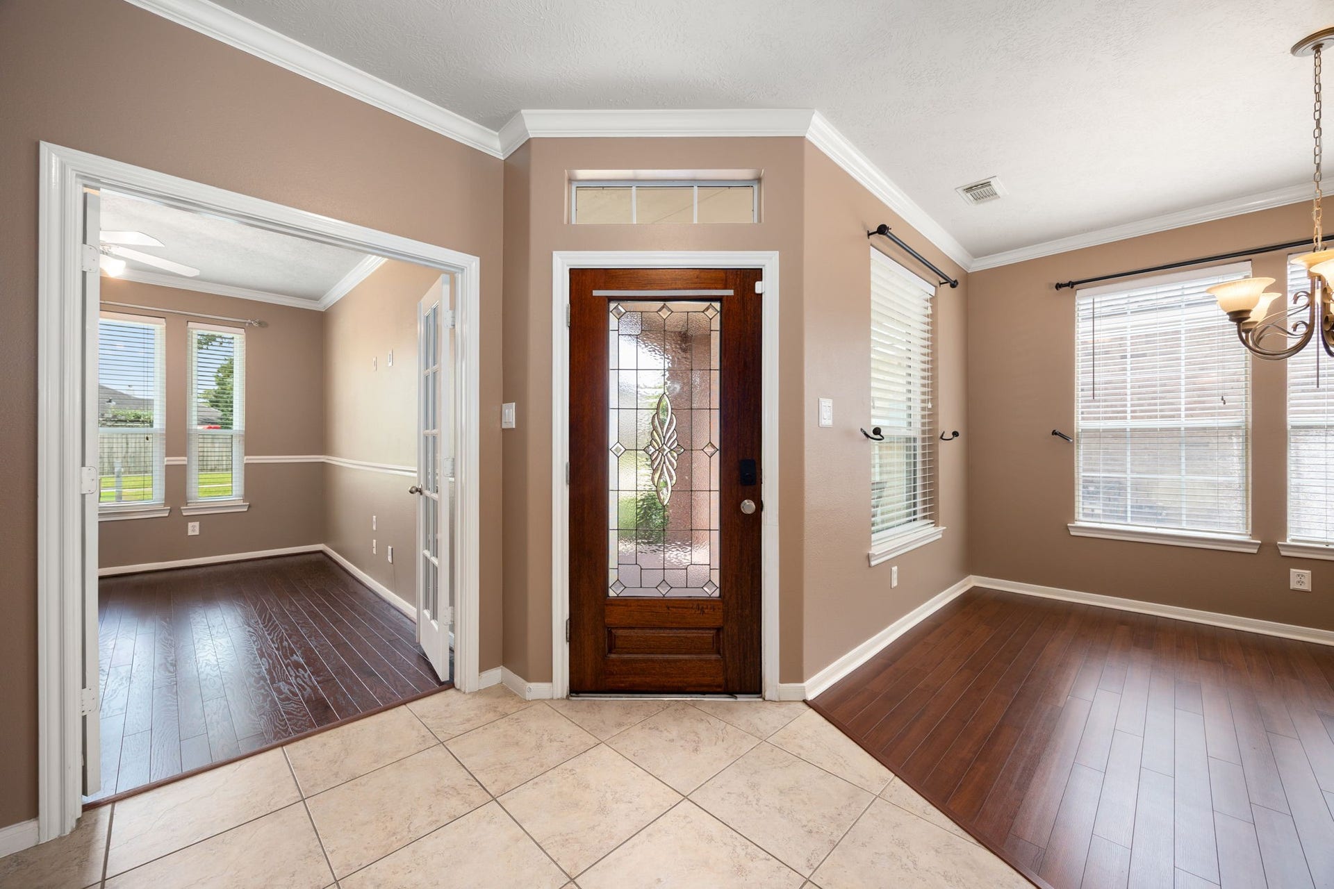 The expansive entryway flows effortlessly into versatile living spaces. To the left, elegant French doors open into a private home office or study with rich wood-look flooring, while a bright formal dining room sits opposite.