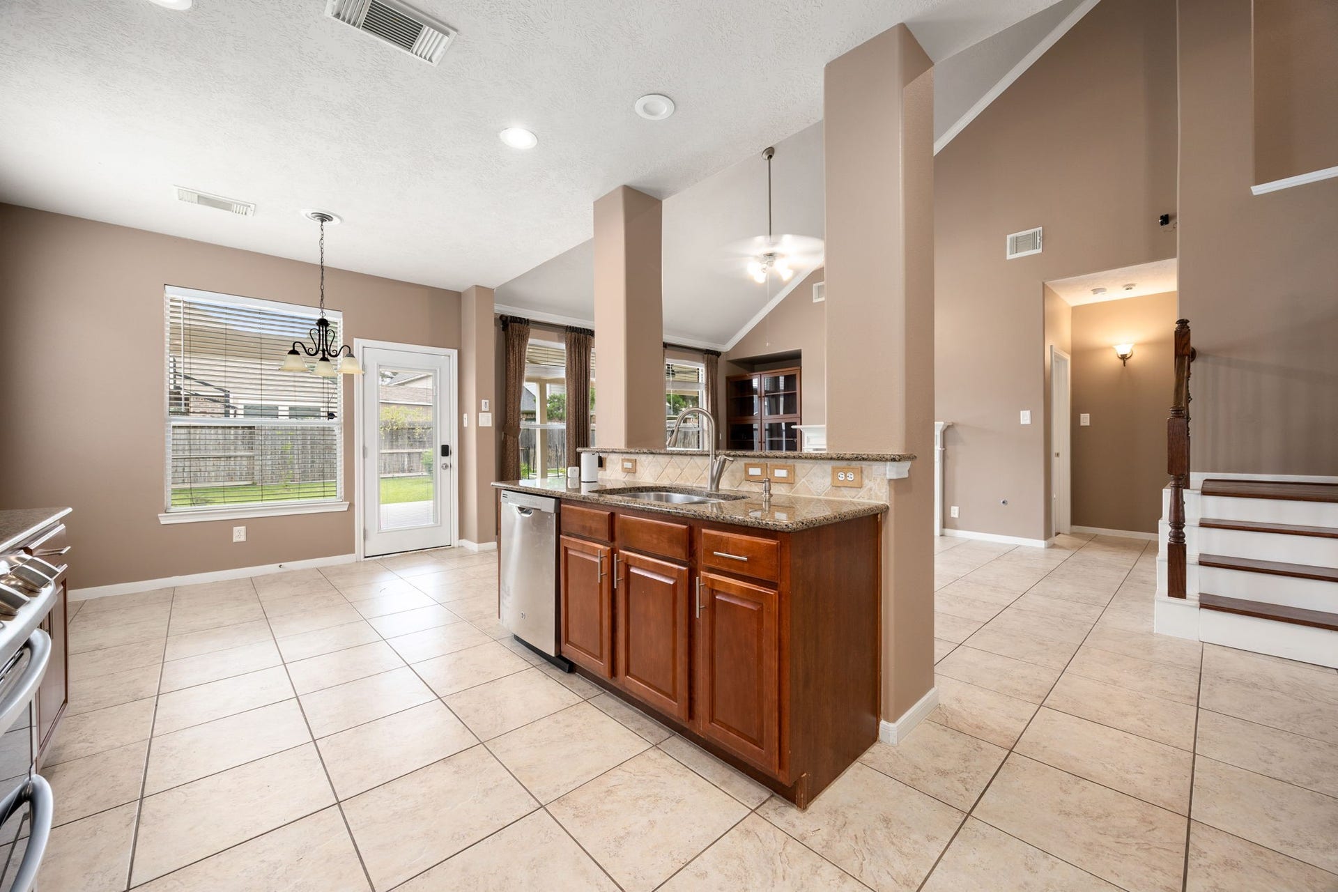 Functional kitchen island overlooking a sunlit breakfast nook with direct backyard access and durable tile flooring throughout.