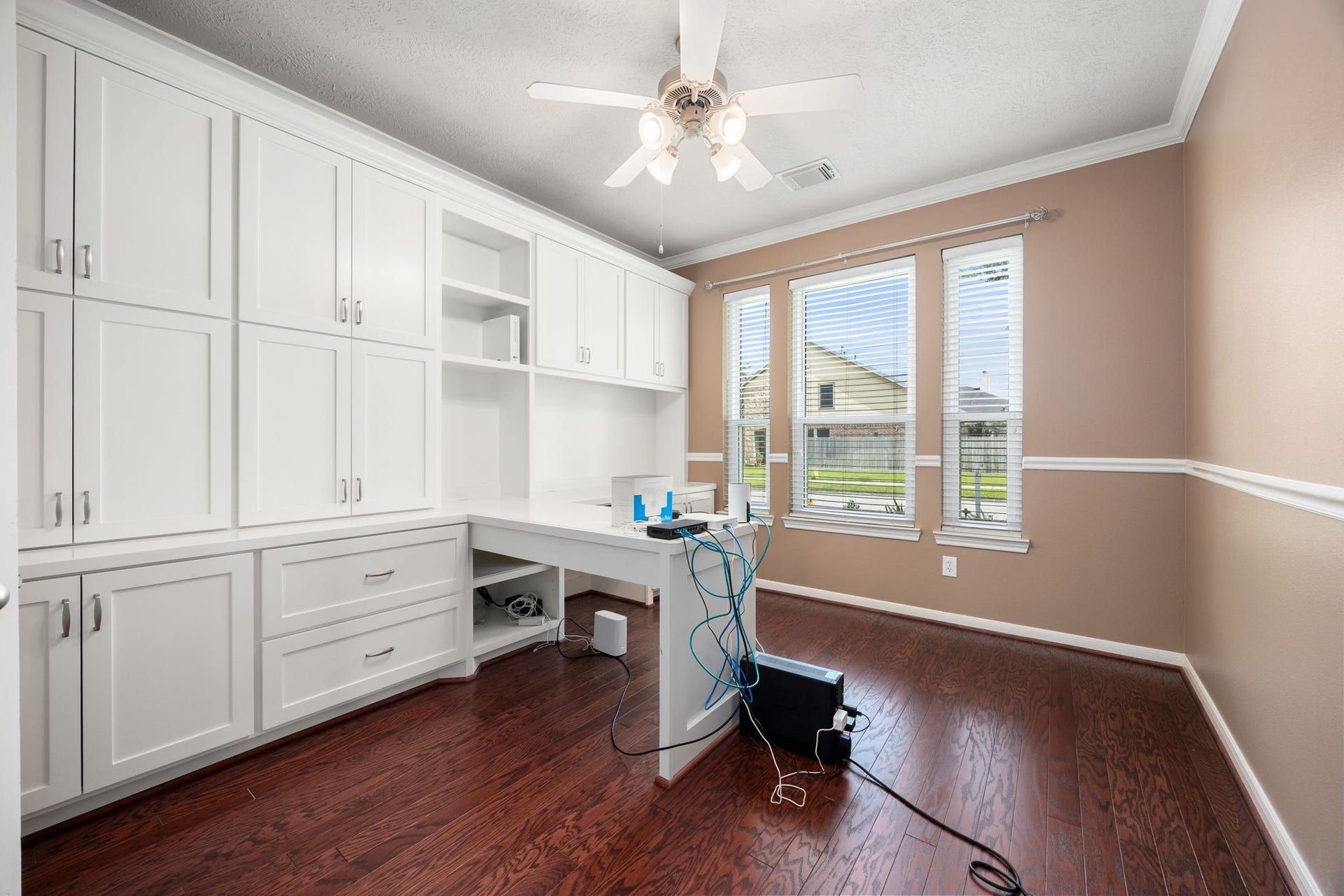 Ideal for remote work or study, this private home office features extensive custom built-in cabinetry, an integrated desk, and abundant storage. Rich wood-look flooring, elegant crown molding, and multiple front-facing windows create a bright and productive workspace.