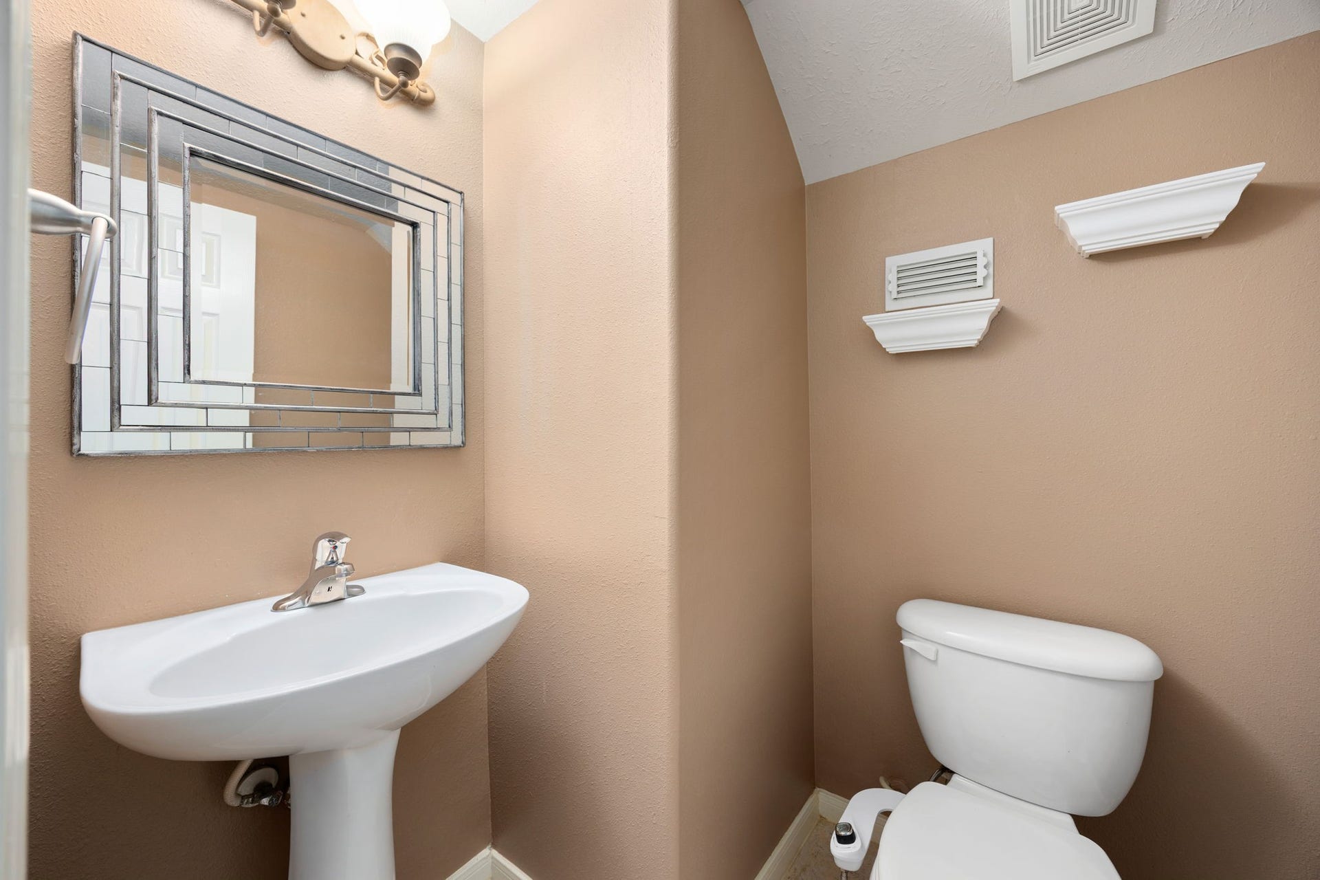 Convenient first-floor powder room perfect for guests, featuring a classic white pedestal sink and a modern chrome faucet. The space is upgraded with a striking, multi-layered statement mirror.