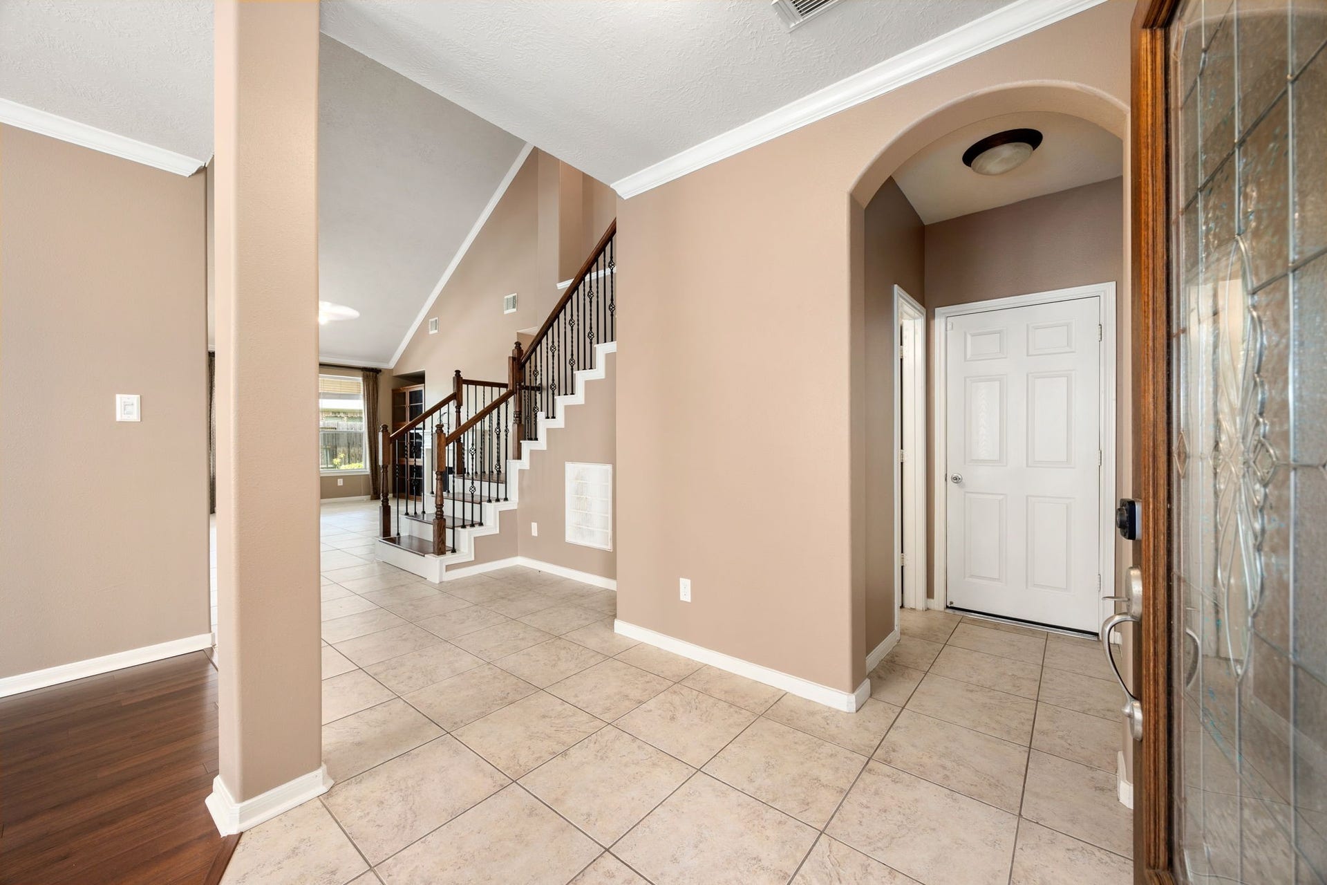 Step inside a grand, welcoming foyer featuring tile flooring, elegant crown molding, and an architectural arched entryway. The spacious entry opens seamlessly to the main living areas and a striking staircase with wrought-iron spindles.