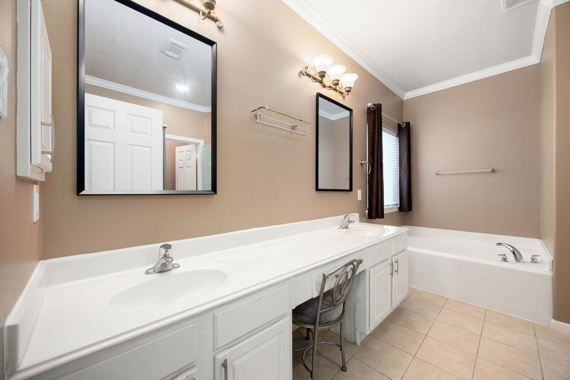 Primary bathroom oasis showcasing a long dual-sink vanity with abundant cabinet storage and modern framed mirrors. A deep soaking tub sits tucked under a window, offering a perfect spot to unwind at the end of the day.
