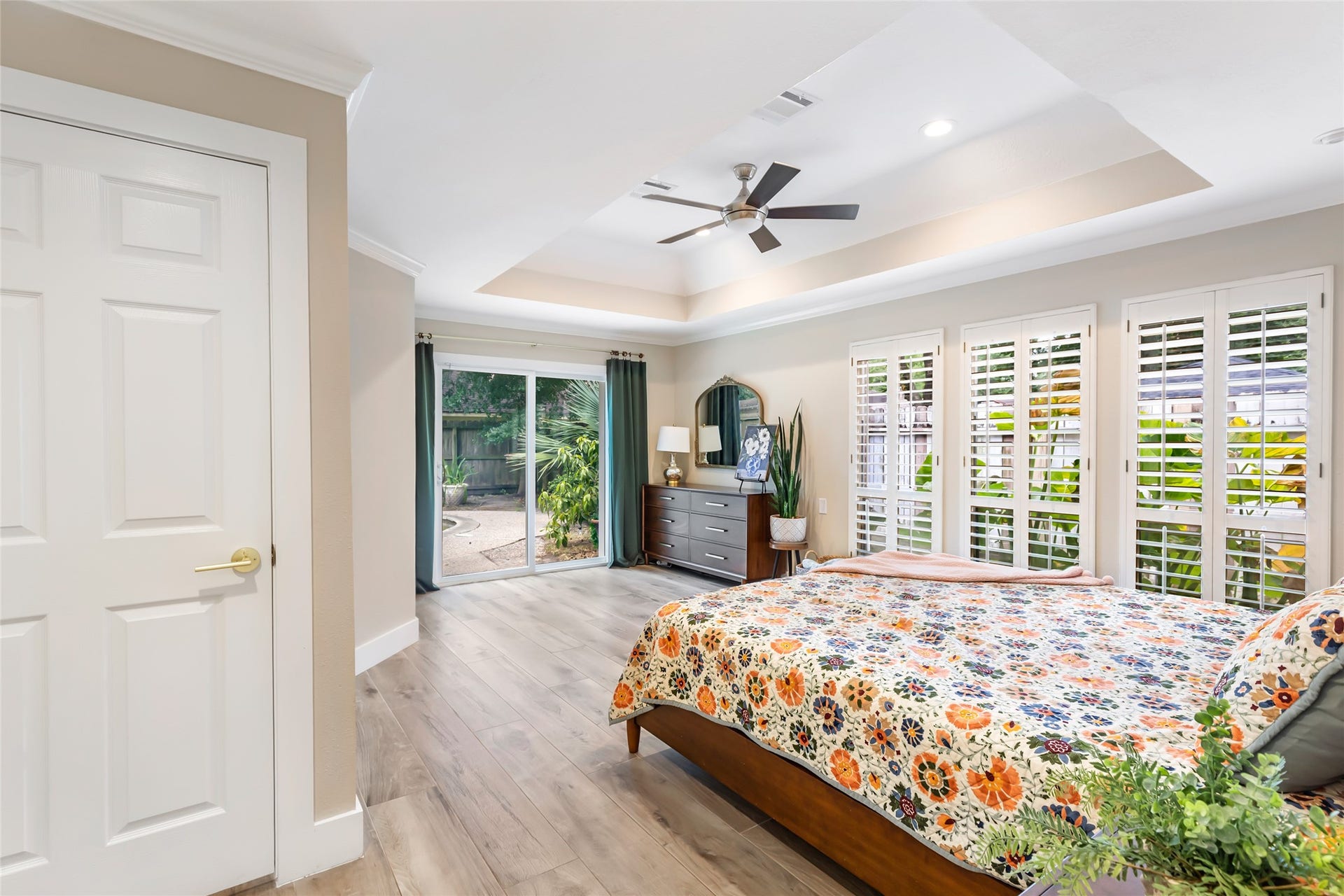 3714 Swift Creek Drive, Kingwood, TX 77339 Spacious and bright primary bedroom featuring elegant tray ceilings and a modern ceiling fan, with large windows and sliding glass doors leading to a lush outdoor area, offering an inviting and serene retreat.