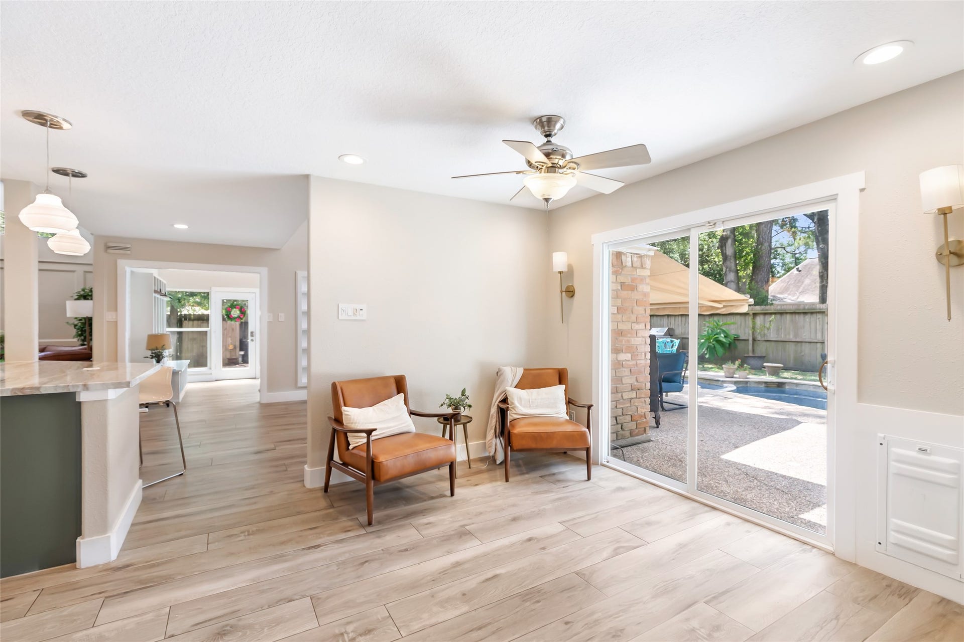 3714 Swift Creek Drive, Kingwood, TX 77339 Bright and inviting versatile living space with stylish wood flooring, cozy seating, and large sliding glass doors leading to a charming outdoor patio and pool area.
