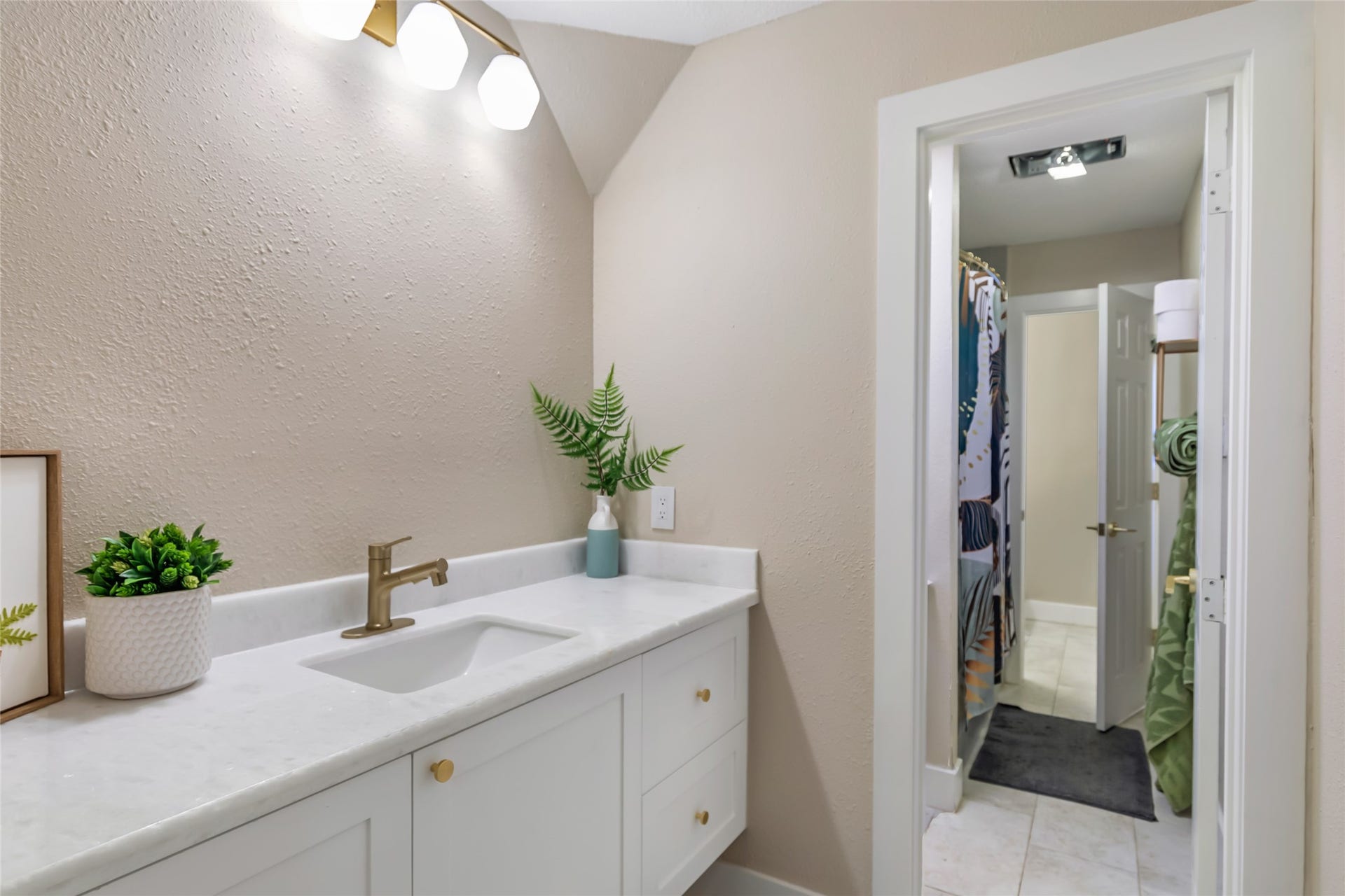 3714 Swift Creek Drive, Kingwood, TX 77339 Modern jack-and-jill bathroom with a sleek white vanity, elegant gold fixtures, and soft lighting, leading to a well-lit shower area.