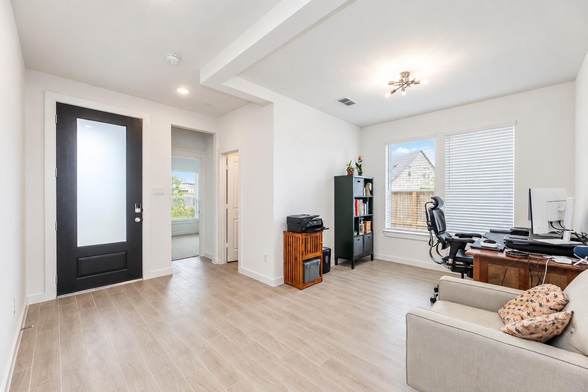 16922 Warm Glow Court, Hockley, TX 77447 Bright and spacious office area with wood-look flooring, large windows for ample natural light, and a sleek modern front door. Perfect for a productive work-from-home setup.