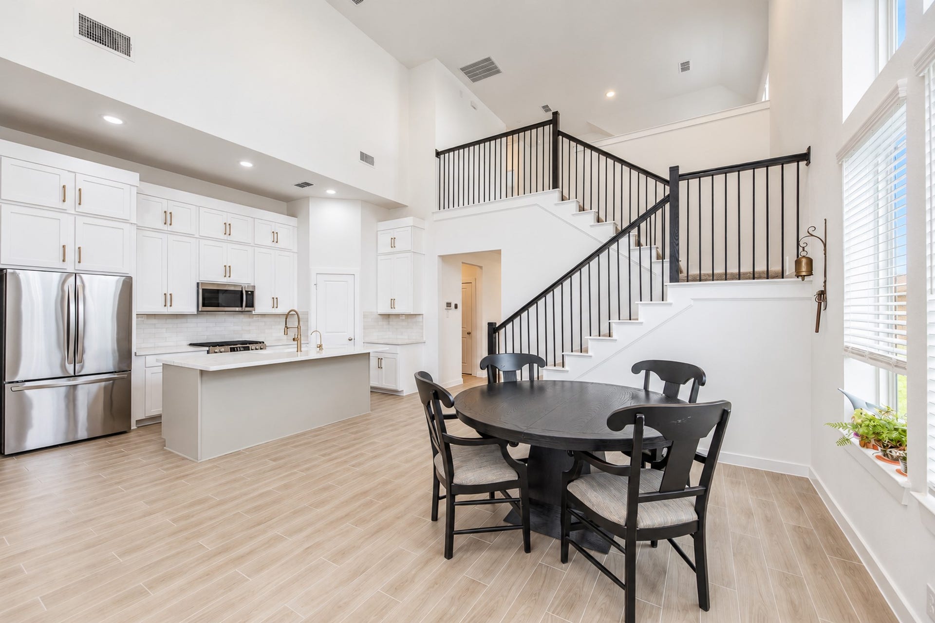 16922 Warm Glow Court, Hockley, TX 77447 Spacious open-concept kitchen and dining area featuring high ceilings, modern cabinetry, stainless steel appliances, and a sleek island, complemented by a stylish staircase and large windows for natural light.
