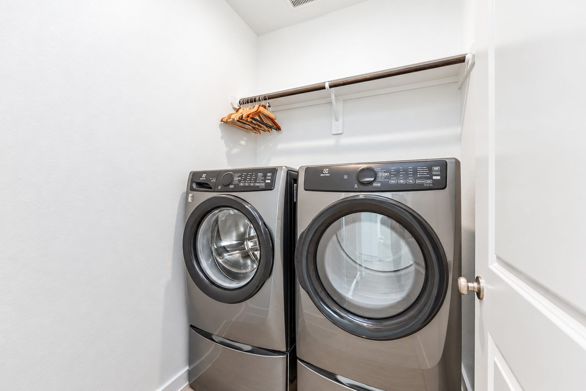 16922 Warm Glow Court, Hockley, TX 77447 Modern laundry room featuring sleek front-loading washer and dryer, complemented by a convenient overhead shelf with hangers.